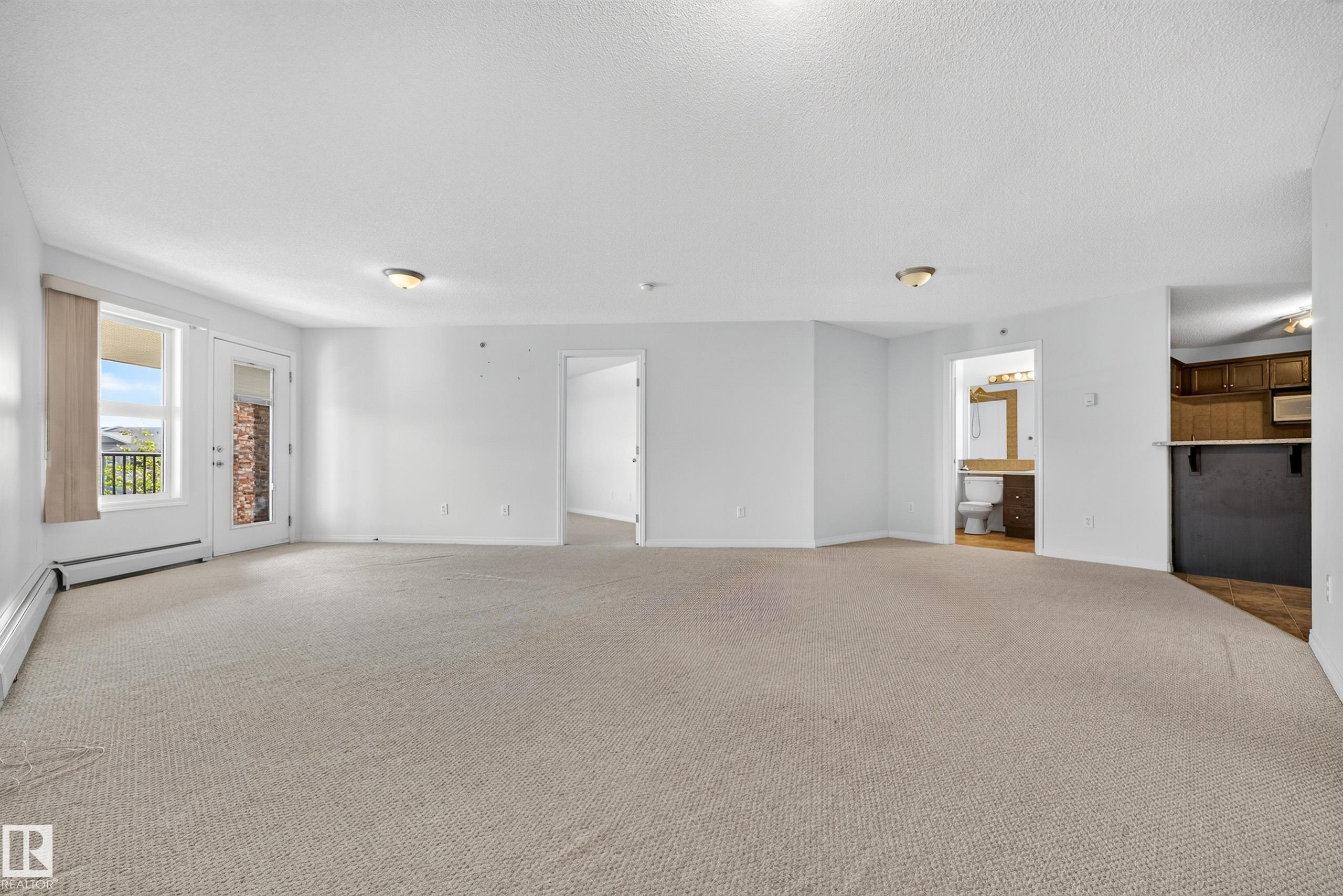 Neutral-toned wall-to-wall carpeting throughout, white painted walls, a glass paneled exterior door with an adjacent window, and a built-in counter with dark cabinetry - #6430 7331 South Terwillegar Dr Nw, Edmonton, AB