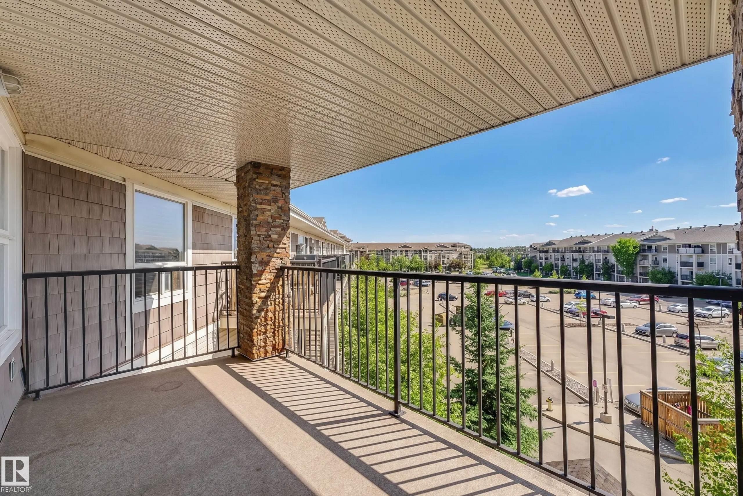 Exterior balcony featuring a stone-clad pillar, black metal railing, and textured siding - #6430 7331 South Terwillegar Dr Nw, Edmonton, AB