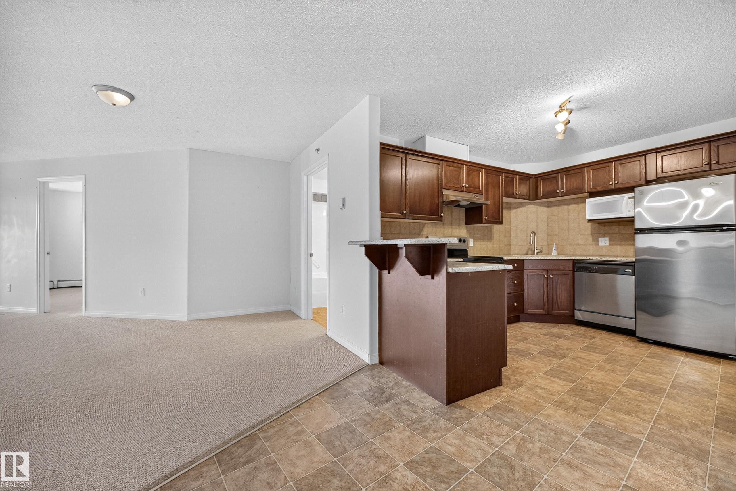 Kitchen featuring wood-finish cabinetry, stainless steel appliances, a tile backsplash, and a breakfast bar - #6430 7331 South Terwillegar Dr Nw, Edmonton, AB