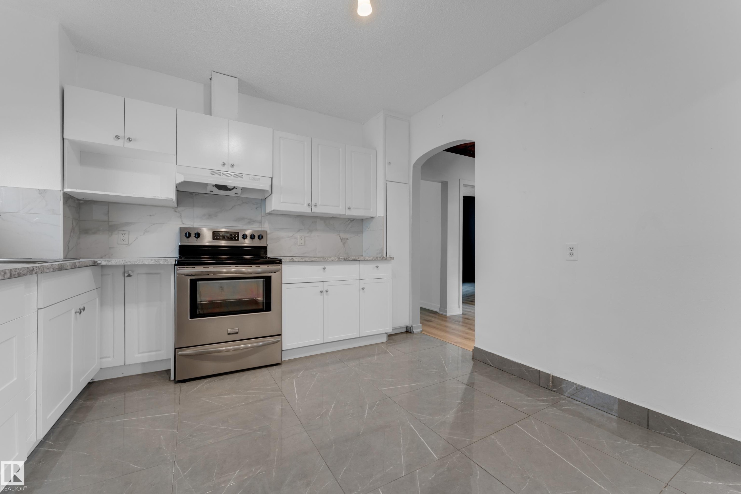 Modern kitchen featuring stainless steel range, white shaker-style cabinetry, light-toned backsplash, and gray tile flooring - 12116 81 Street Nw, Edmonton, AB