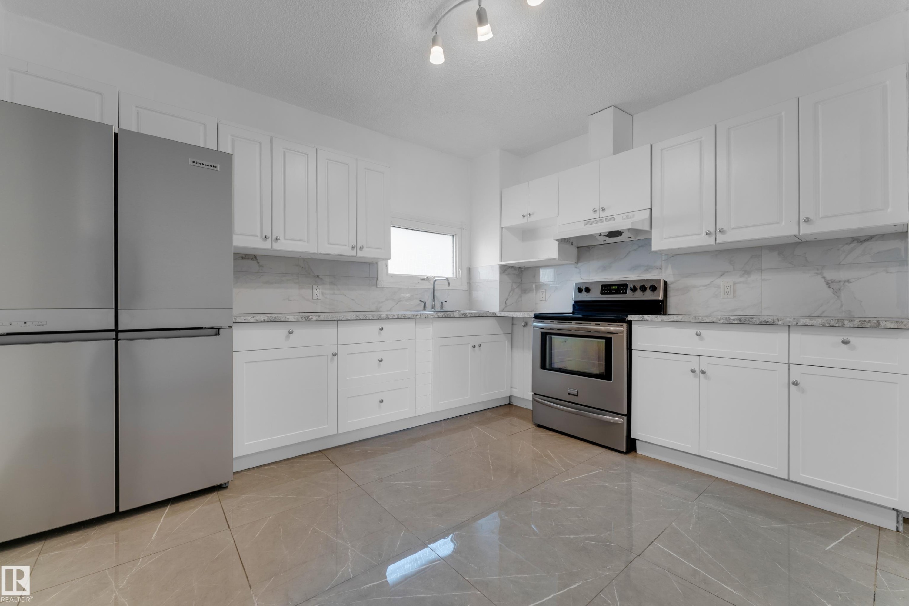 Kitchen featuring white shaker-style cabinetry, stainless steel appliances, stone countertops, a tile backsplash, and large format tile flooring - 12116 81 Street Nw, Edmonton, AB