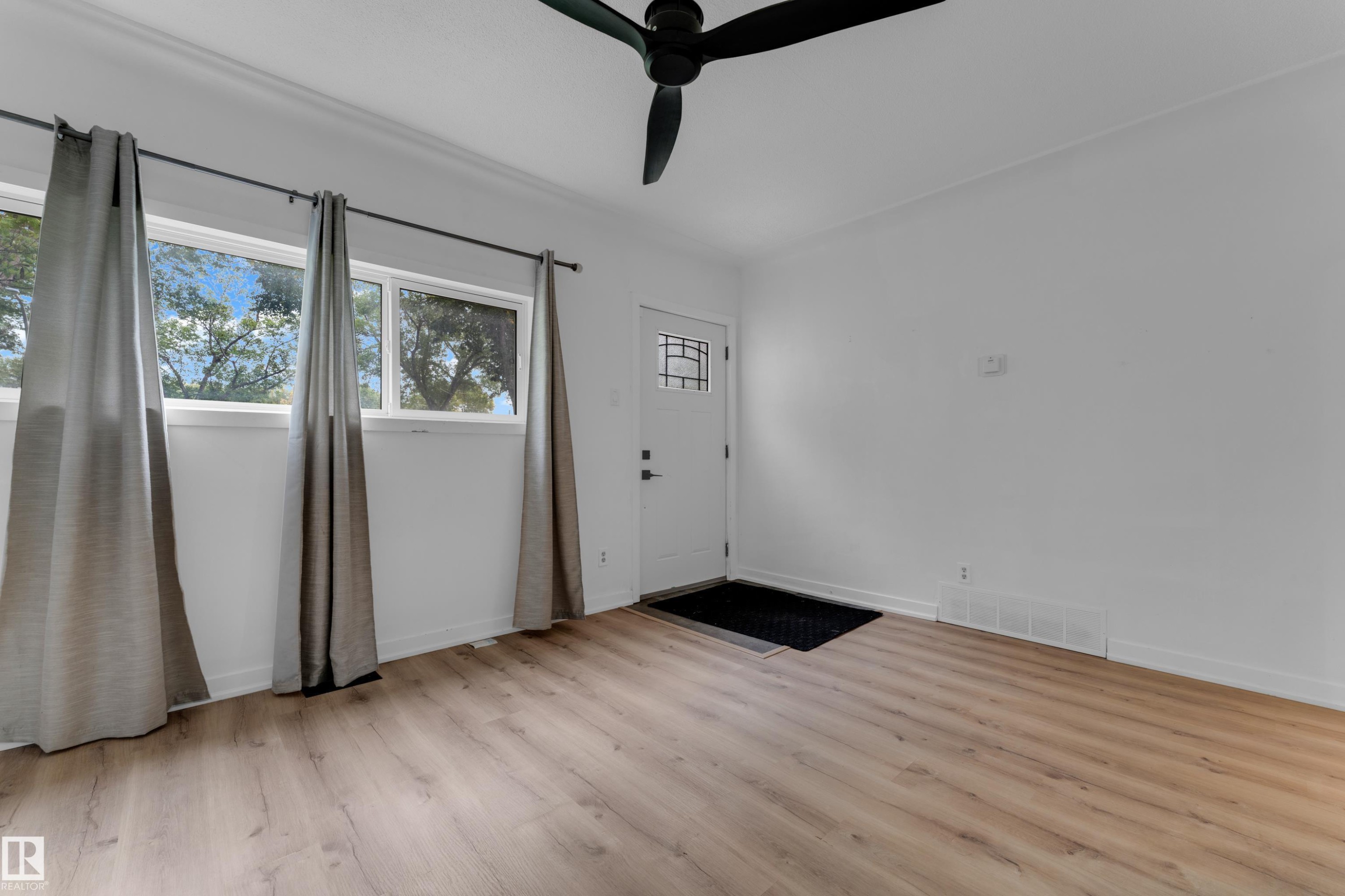 Wood-finish flooring, two large windows, a ceiling fan, and a front entry door with decorative glass - 12116 81 Street Nw, Edmonton, AB