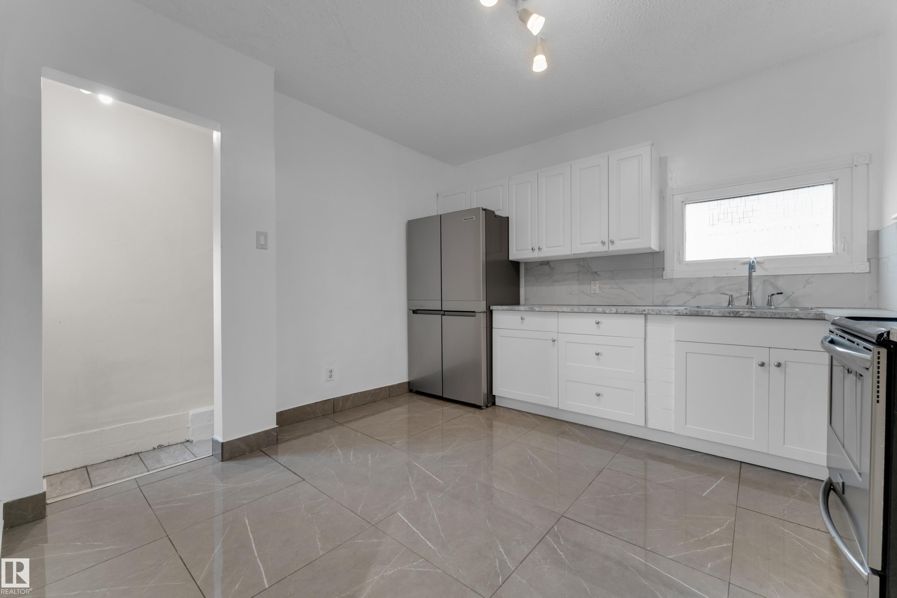 Grey-toned tile flooring, white shaker cabinetry, stainless steel appliances, white countertop, and a white tile backsplash - 12116 81 Street Nw, Edmonton, AB