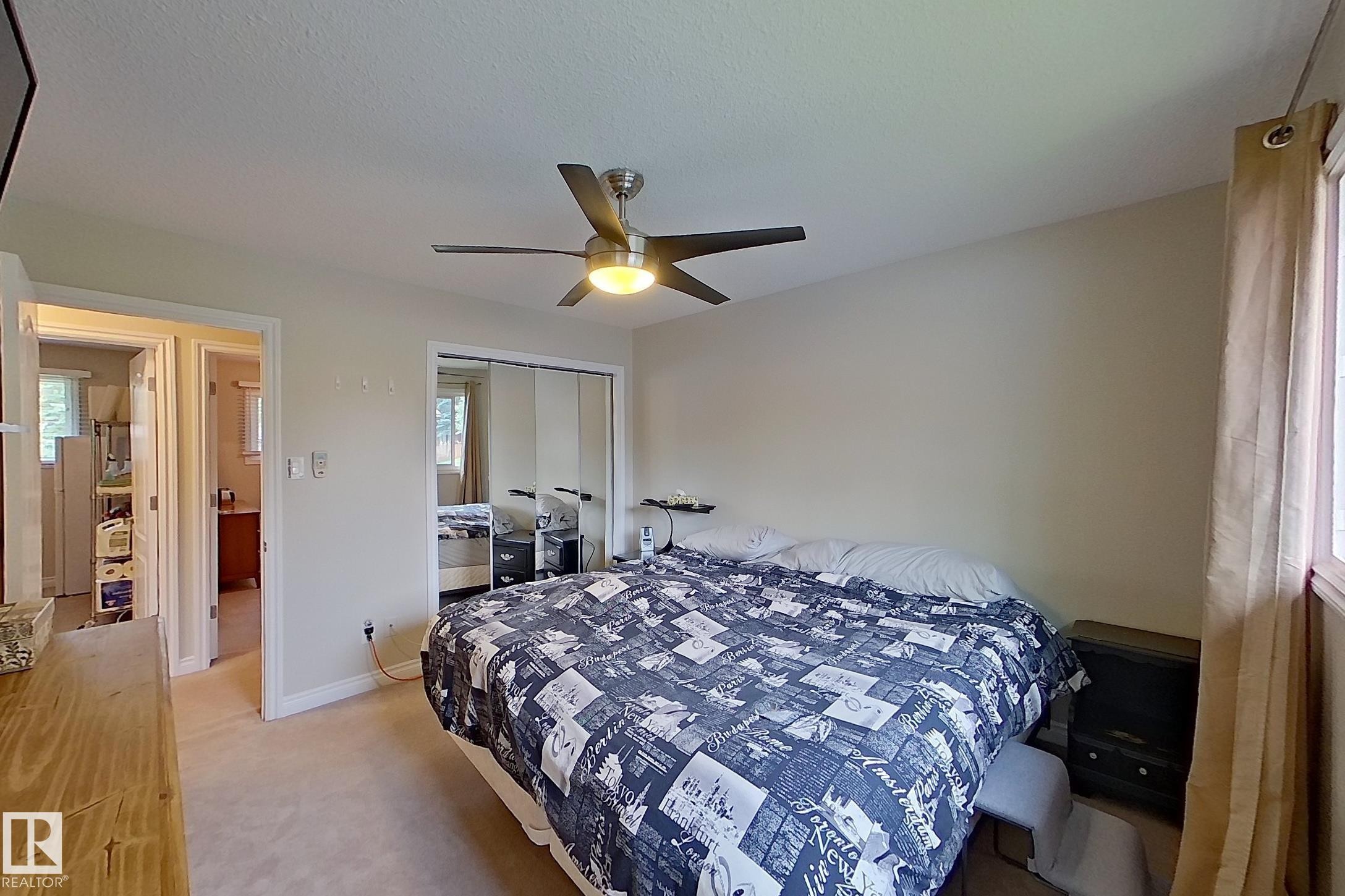 Spacious primary bedroom featuring wood-finish flooring, mirrored closet doors, ceiling fan with integrated lighting, and abundant natural light from windows - 14 Brunswick Crescent, St. Albert, AB