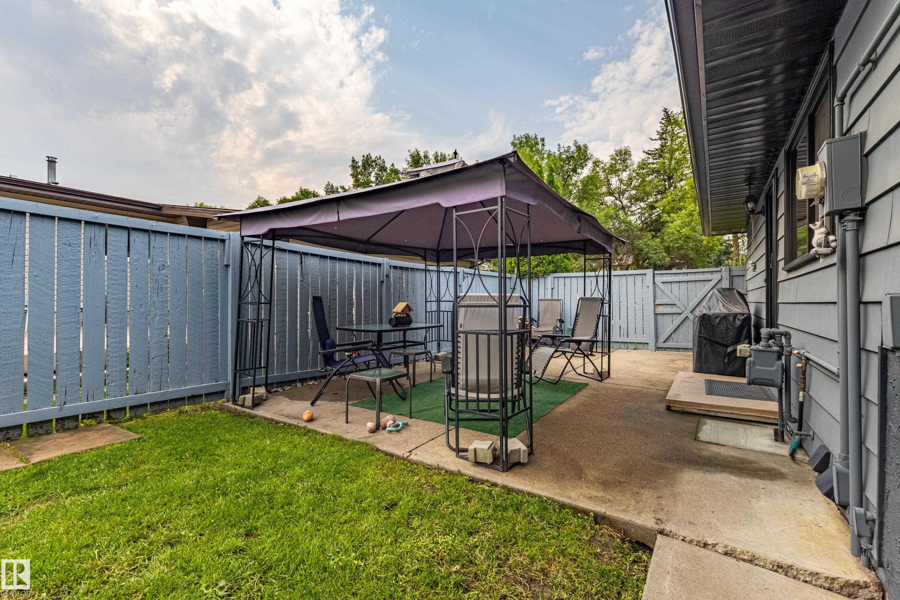 Spacious backyard oasis featuring a covered patio structure with integrated seating area, manicured lawn, mature landscaping, concrete hardscape, and direct access to the home's exterior - 14 Brunswick Crescent, St. Albert, AB