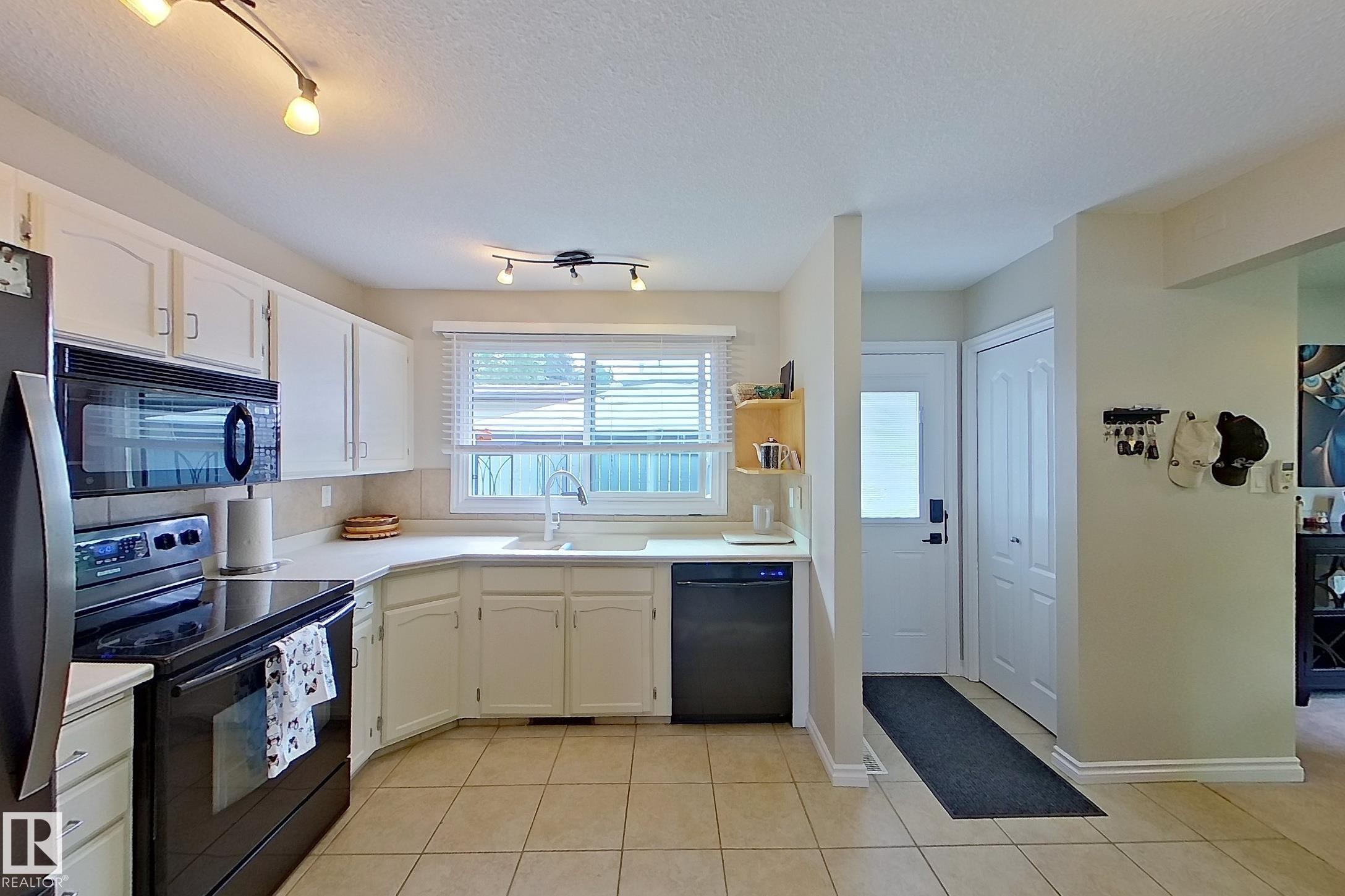 Kitchen featuring white cabinetry, black appliances, track lighting, and tile flooring - 14 Brunswick Crescent, St. Albert, AB