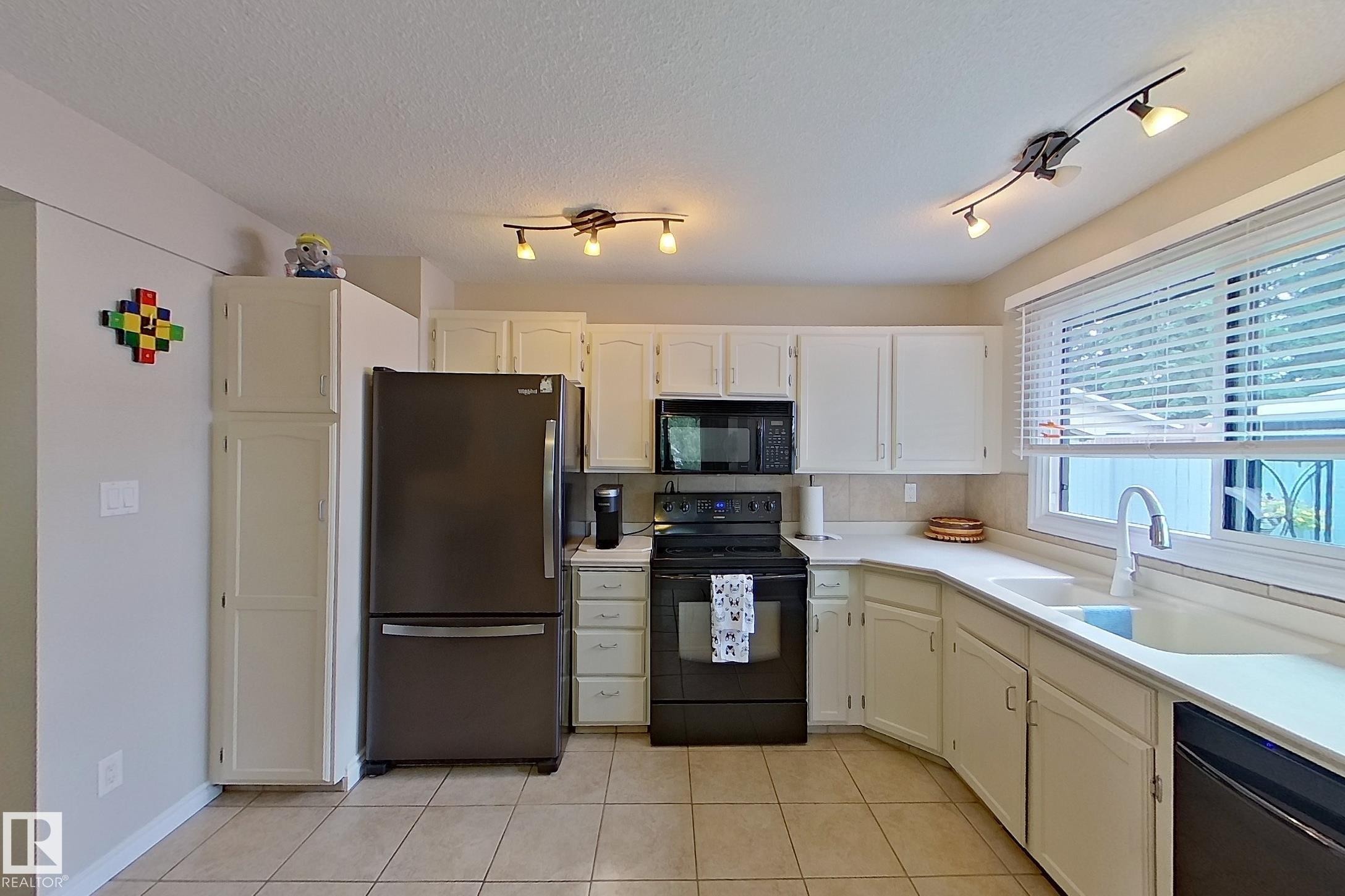 Kitchen featuring white cabinetry, light-toned countertops, a stainless steel refrigerator, black range, and an undermount sink - 14 Brunswick Crescent, St. Albert, AB