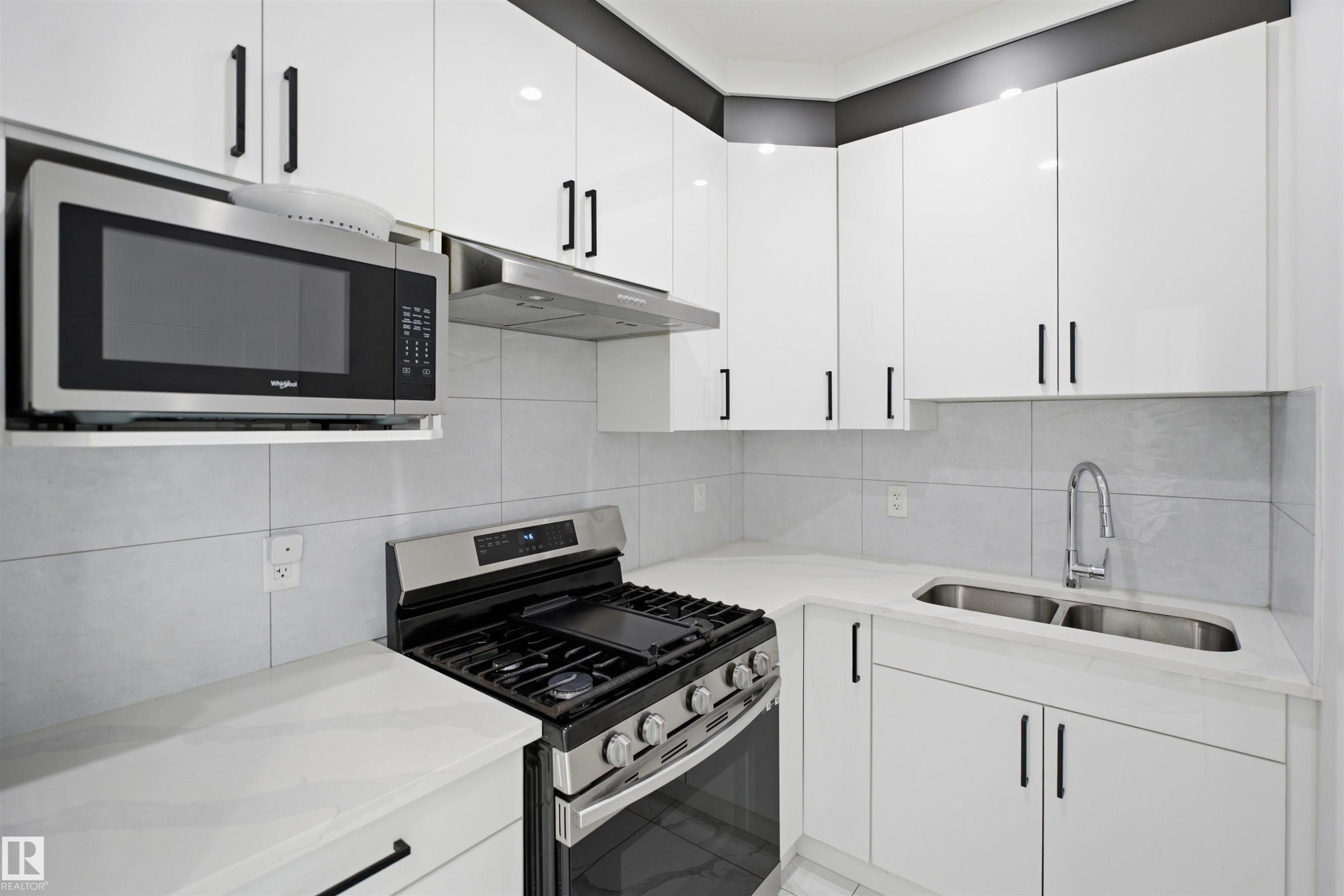 White cabinetry with matte black hardware, stainless steel gas range, over-the-range microwave, dual basin undermount sink, and light-toned countertops - 2027 13 Avenue Nw, Edmonton, AB