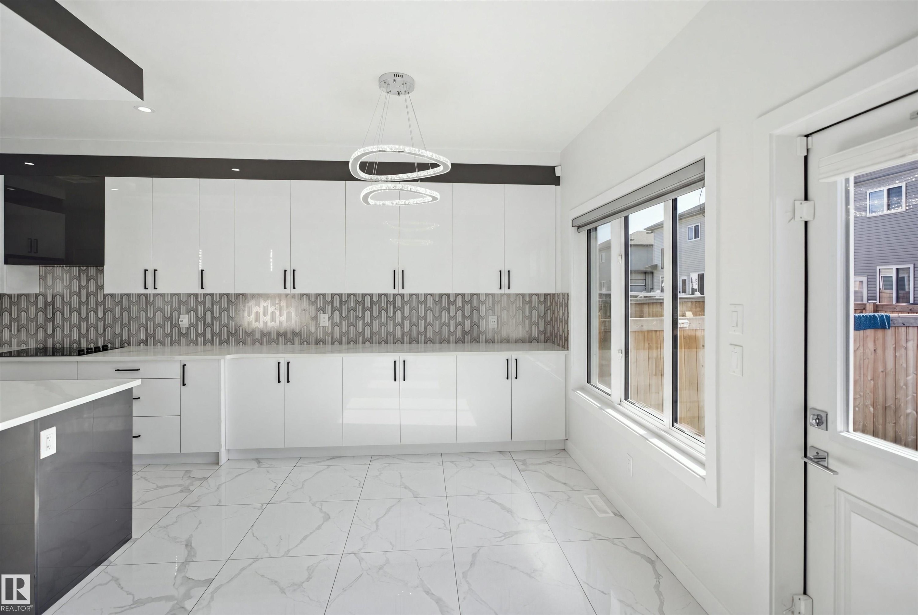 Sleek kitchen featuring white gloss cabinetry, a patterned tile backsplash, recessed lighting, and a contemporary chandelier - 2027 13 Avenue Nw, Edmonton, AB