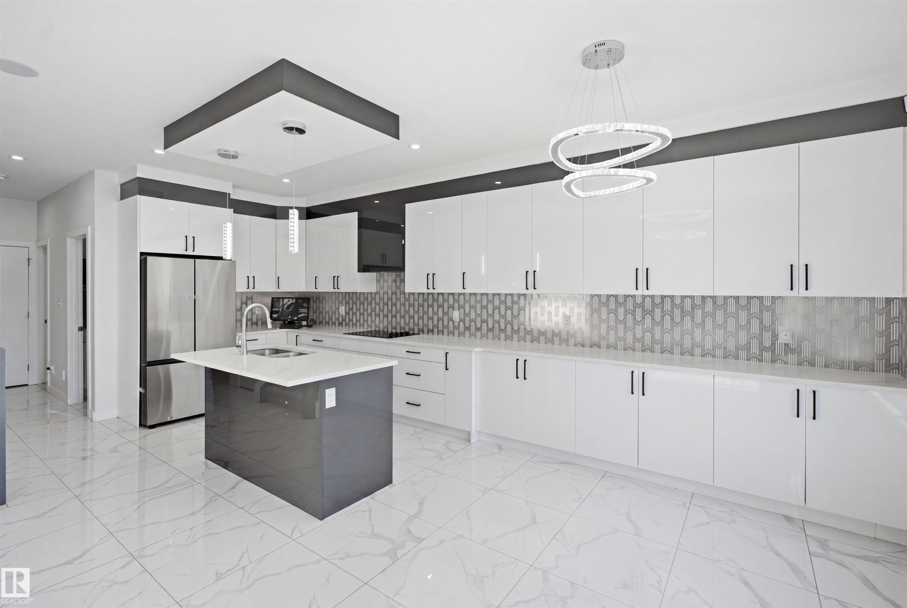 Modern kitchen featuring a central island with a sink, extensive white cabinetry, a tiled backsplash, and stainless steel appliances - 2027 13 Avenue Nw, Edmonton, AB