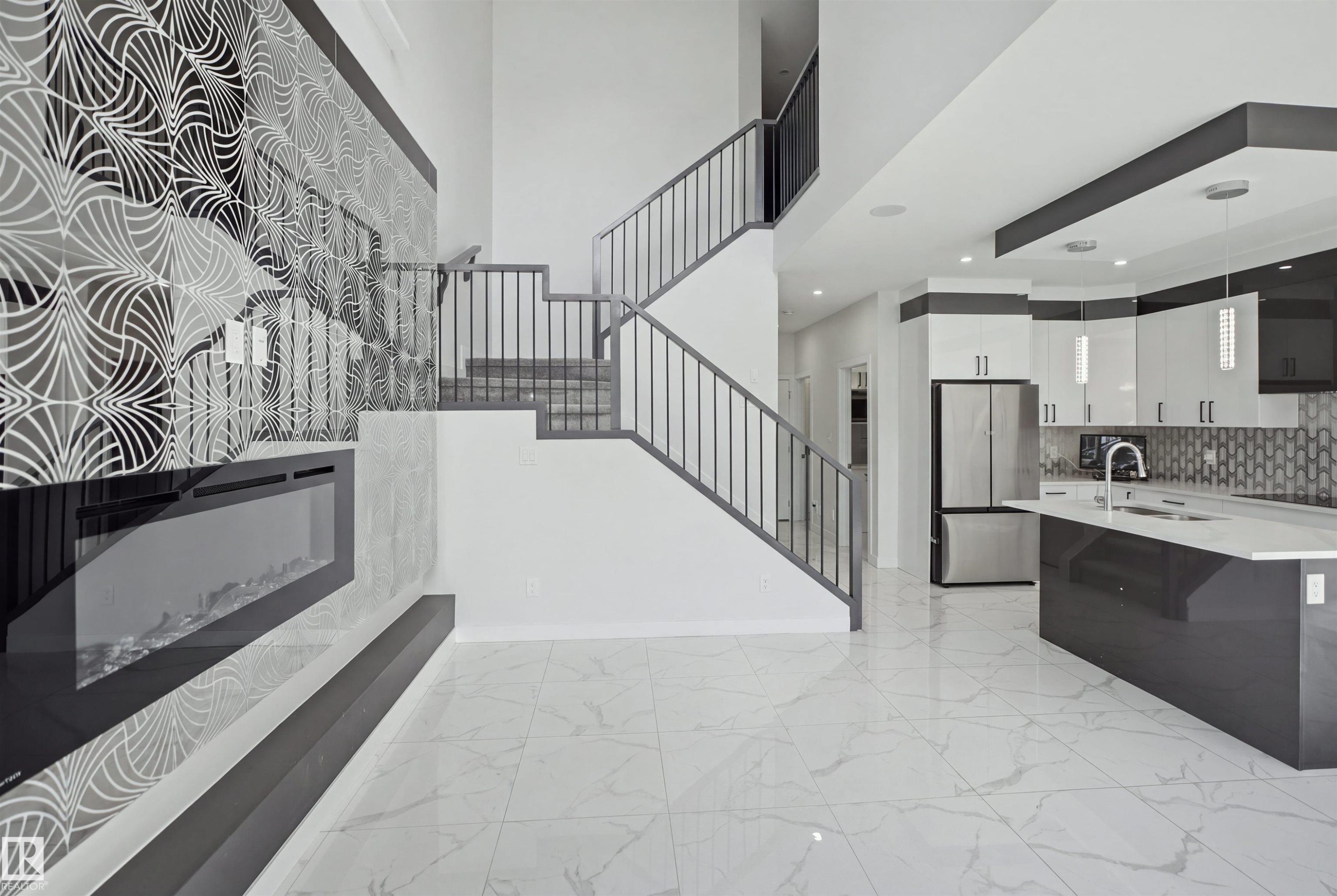 Two-story ceiling, contemporary staircase with metal railings, built-in electric fireplace with decorative accent wall, white tile flooring, and kitchen island with an undermount sink - 2027 13 Avenue Nw, Edmonton, AB