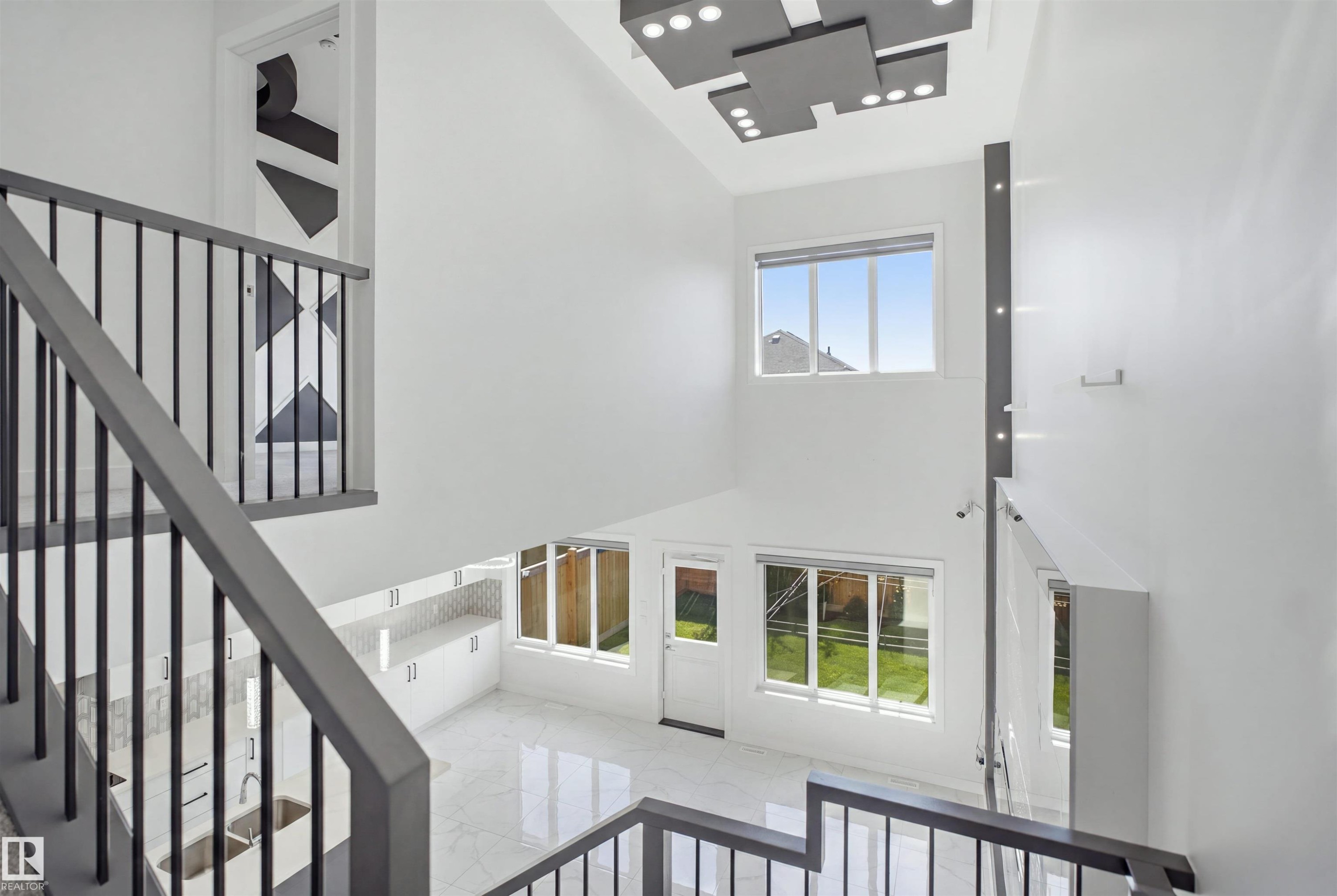 Vaulted ceiling with a contemporary lighting fixture, staircase with metal balusters, white tile flooring, and white cabinetry - 2027 13 Avenue Nw, Edmonton, AB