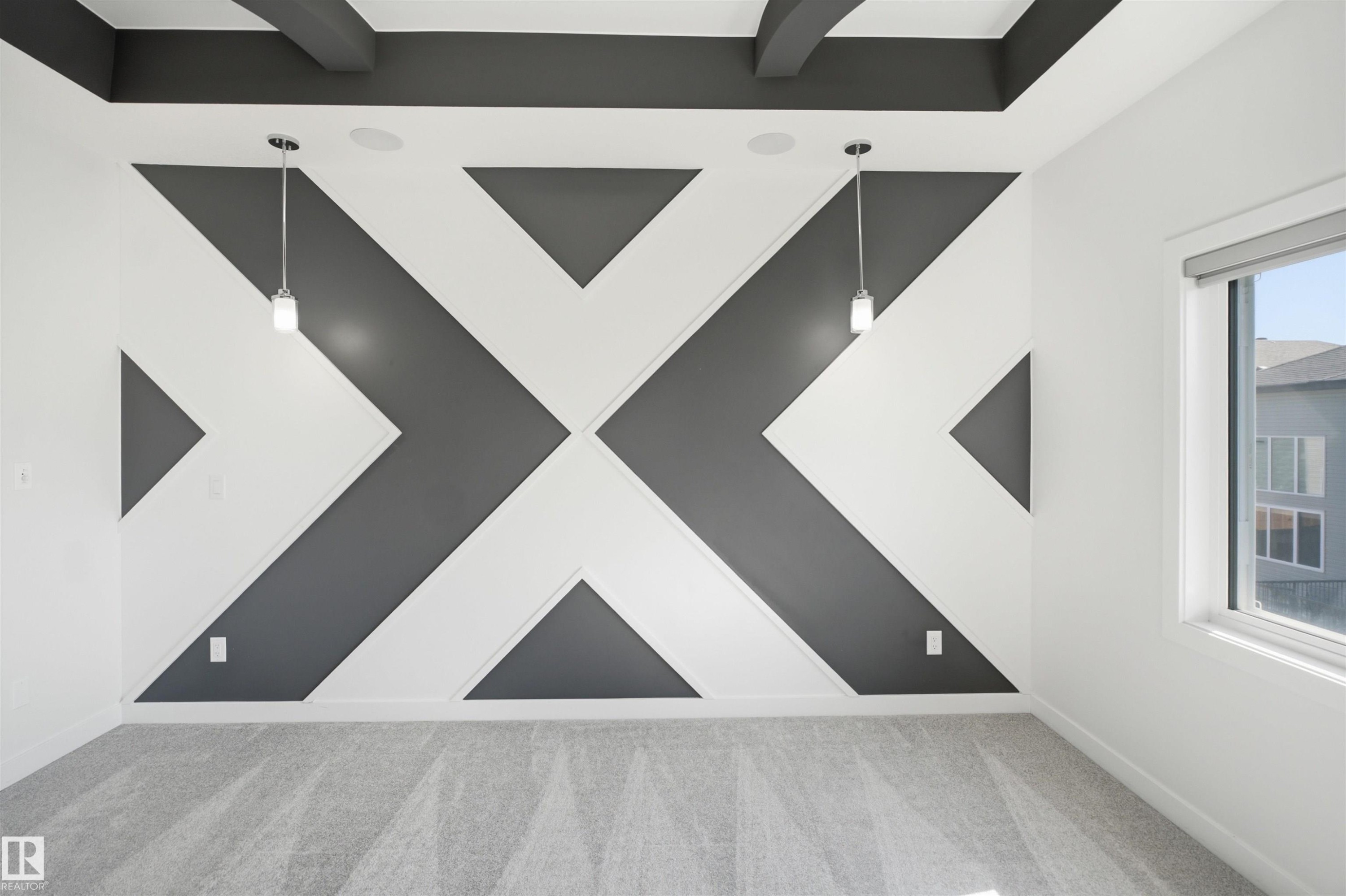 Accent wall with geometric design, suspended pendant lighting, textured carpet flooring, and a large window with roller shade - 2027 13 Avenue Nw, Edmonton, AB