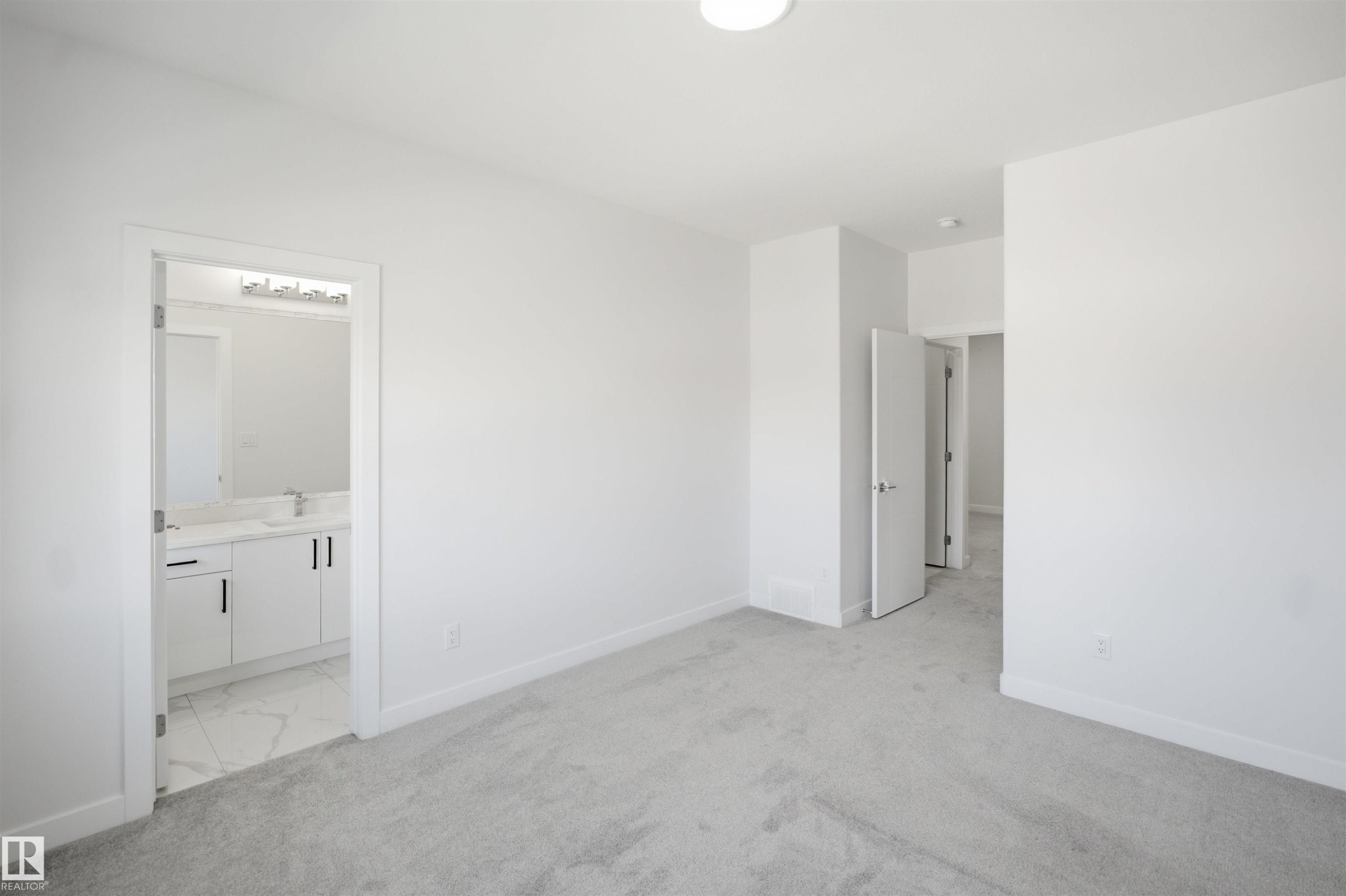 Plush grey carpeting, white interior doors, and a bathroom featuring a white vanity with dark hardware, a rectangular undermount sink, and patterned floor tile - 2027 13 Avenue Nw, Edmonton, AB