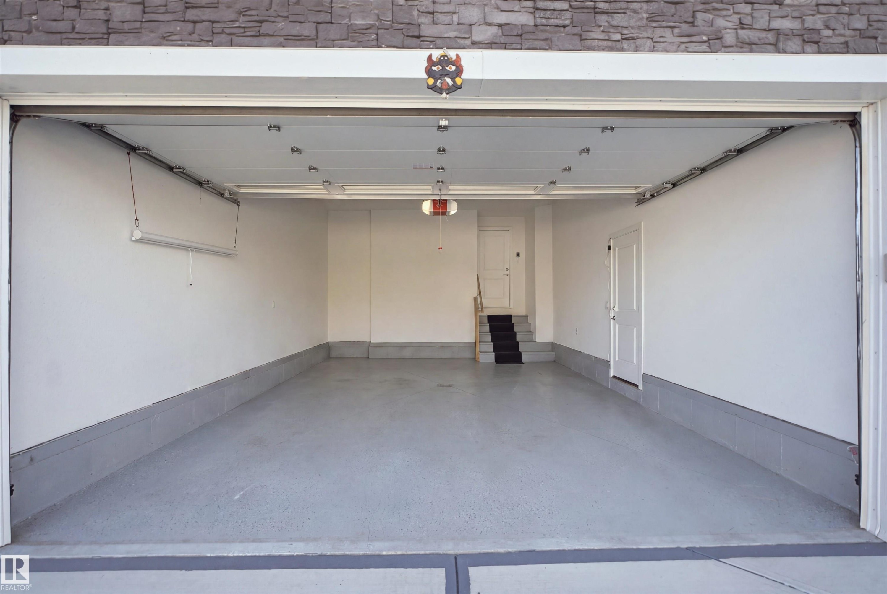 Spacious garage with light gray flooring, white painted walls, white door, and built-in overhead lighting - 2027 13 Avenue Nw, Edmonton, AB