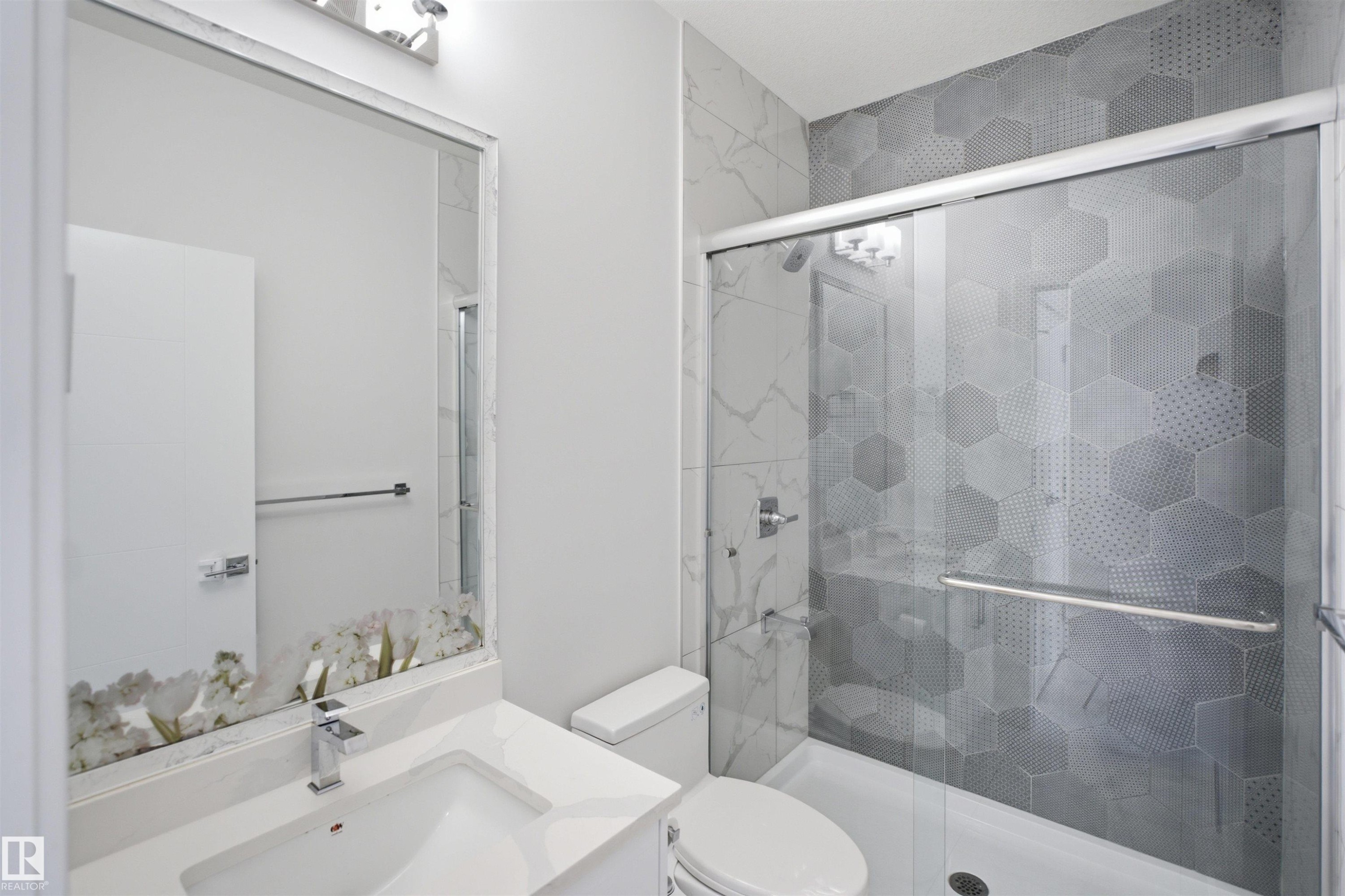 Modern bathroom featuring a glass-enclosed shower, hexagon pattern wall tile, a white vanity with an integrated sink, and a chrome faucet - 2027 13 Avenue Nw, Edmonton, AB