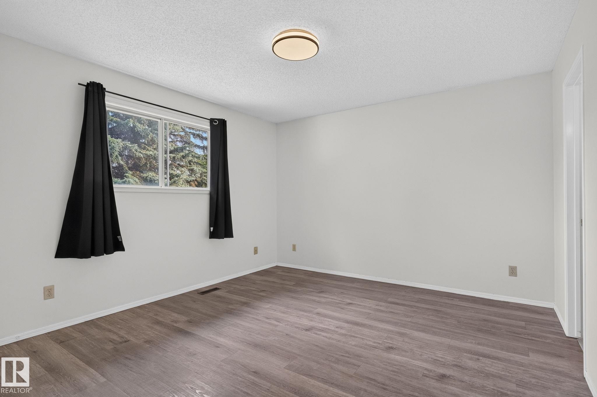 Spacious room featuring wood-finish flooring and a large window - 3722 34A Avenue Nw, Edmonton, AB - Indoor Photo Showing Other Room
