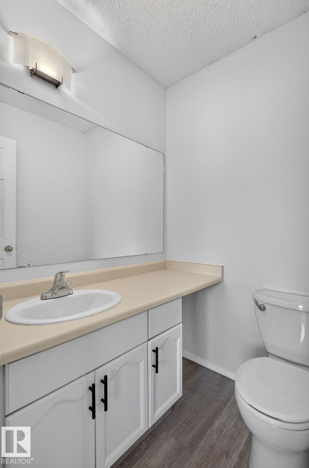 Bathroom featuring a white vanity with black hardware, an integrated sink, a large wall-mounted mirror, and wood-finish flooring - 3722 34A Avenue Nw, Edmonton, AB - Indoor Photo Showing Bathroom