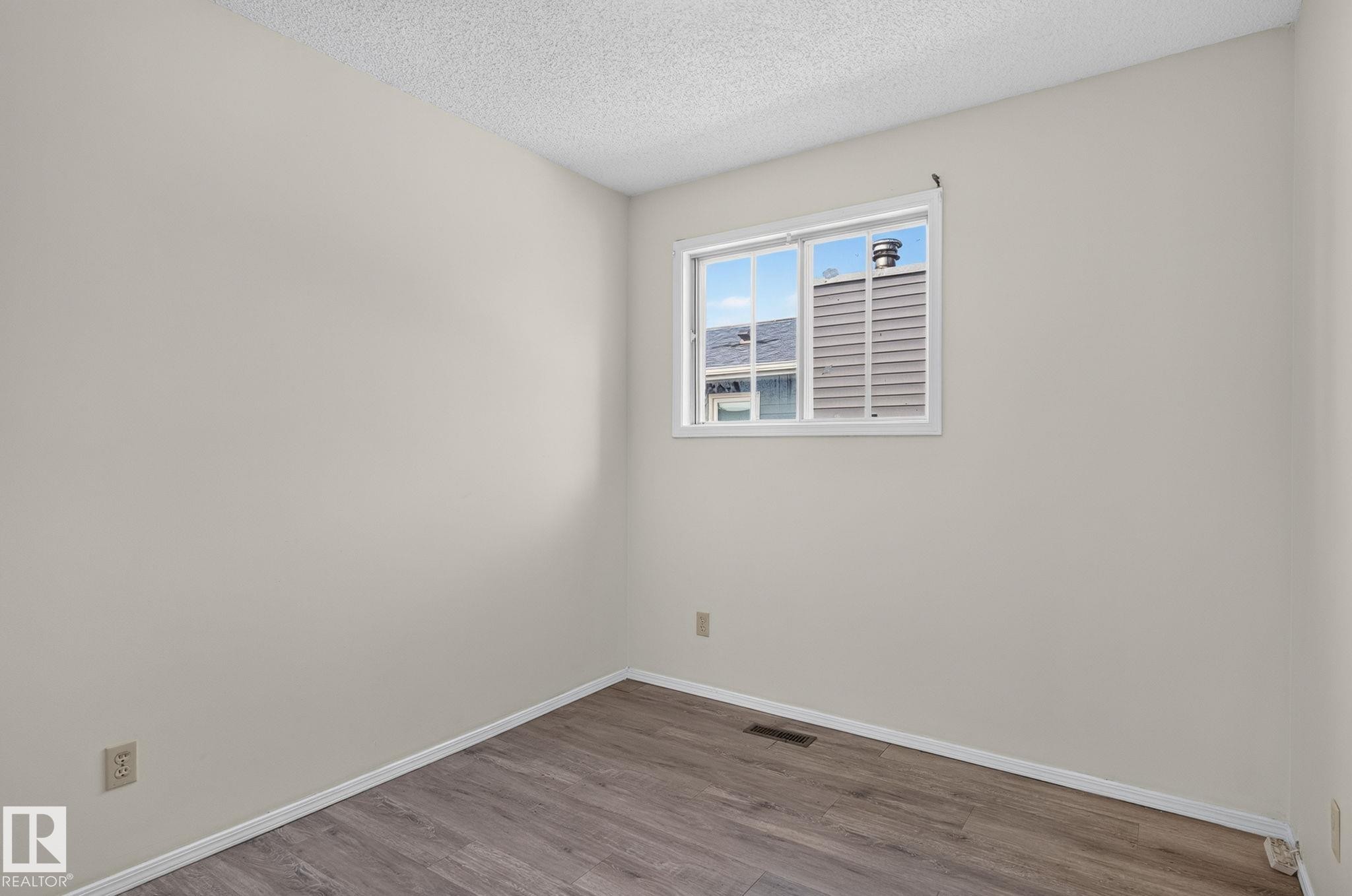 Neutral tone walls with wood-finish flooring, white baseboards, and a white window frame - 3722 34A Avenue Nw, Edmonton, AB - Indoor Photo Showing Other Room