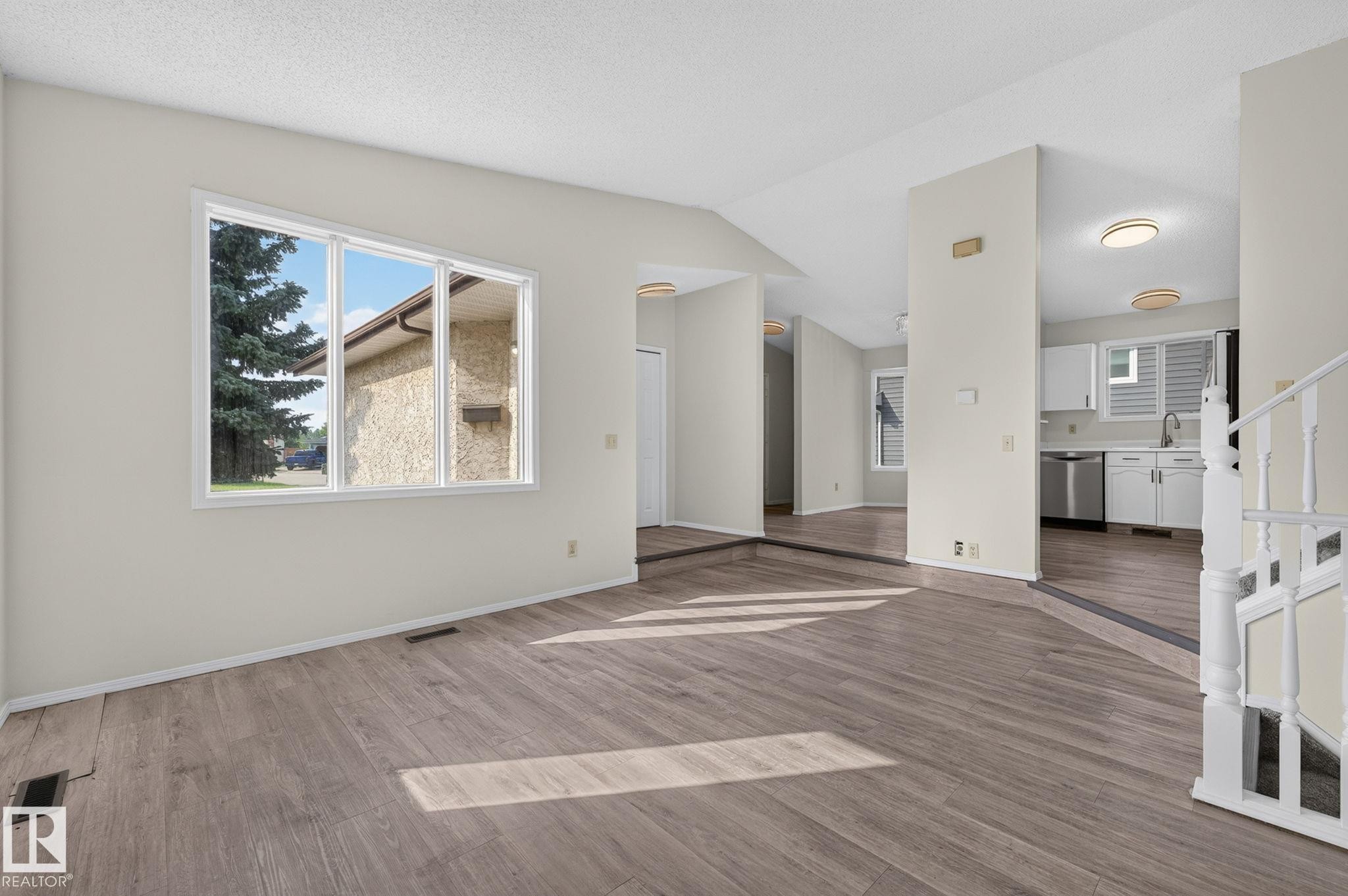 Spacious living area featuring wood-finish flooring, a large multi-pane window, and a crisp white color palette - 3722 34A Avenue Nw, Edmonton, AB - Indoor Photo Showing Other Room
