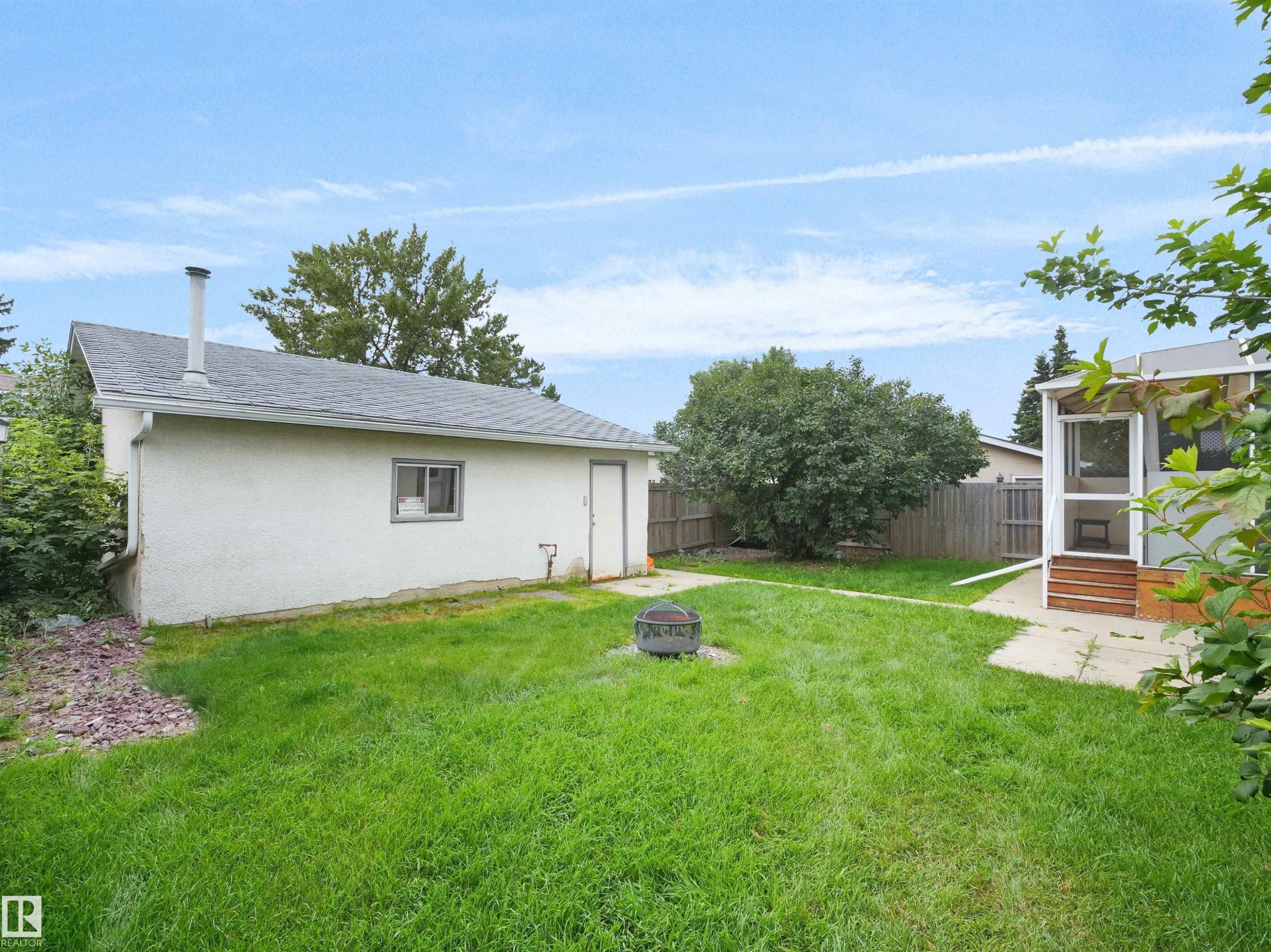 Expansive lawn, detached garage with shingle roof, screened porch with wood-finish steps, concrete patio, and perimeter fencing - 7435 32 Avenue Nw, Edmonton, AB