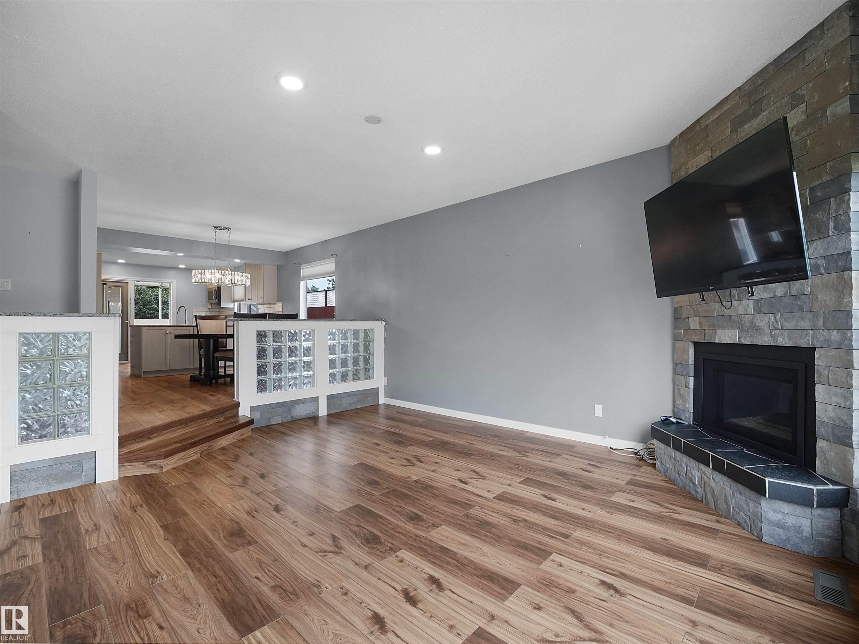 Wood-finish flooring, recessed lighting, stone-clad fireplace, glass block accent walls, and an open-concept design - 7435 32 Avenue Nw, Edmonton, AB
