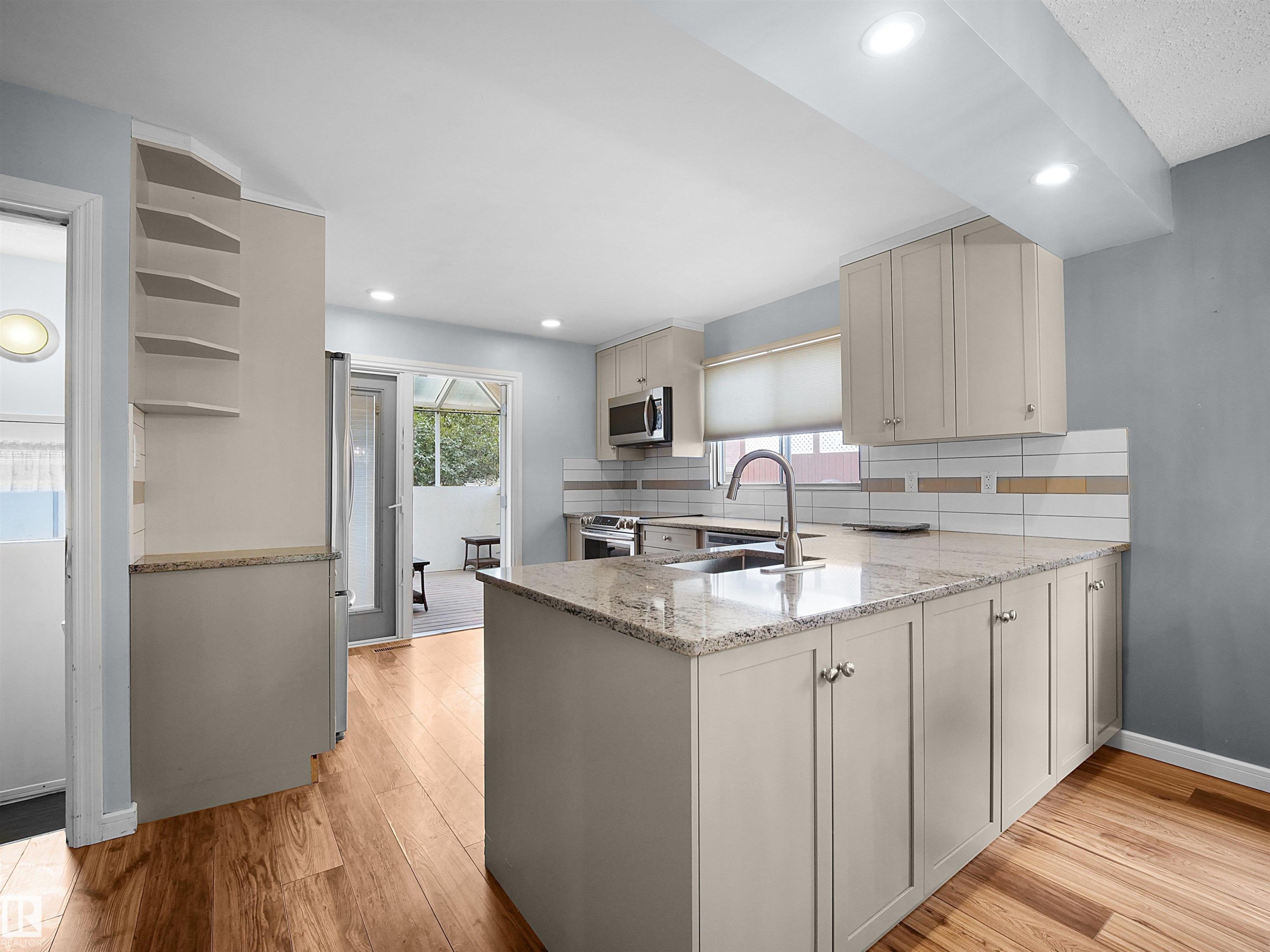 Kitchen featuring wood-finish flooring, granite countertops, white subway tile backsplash with accent strips, and light-toned cabinetry - 7435 32 Avenue Nw, Edmonton, AB