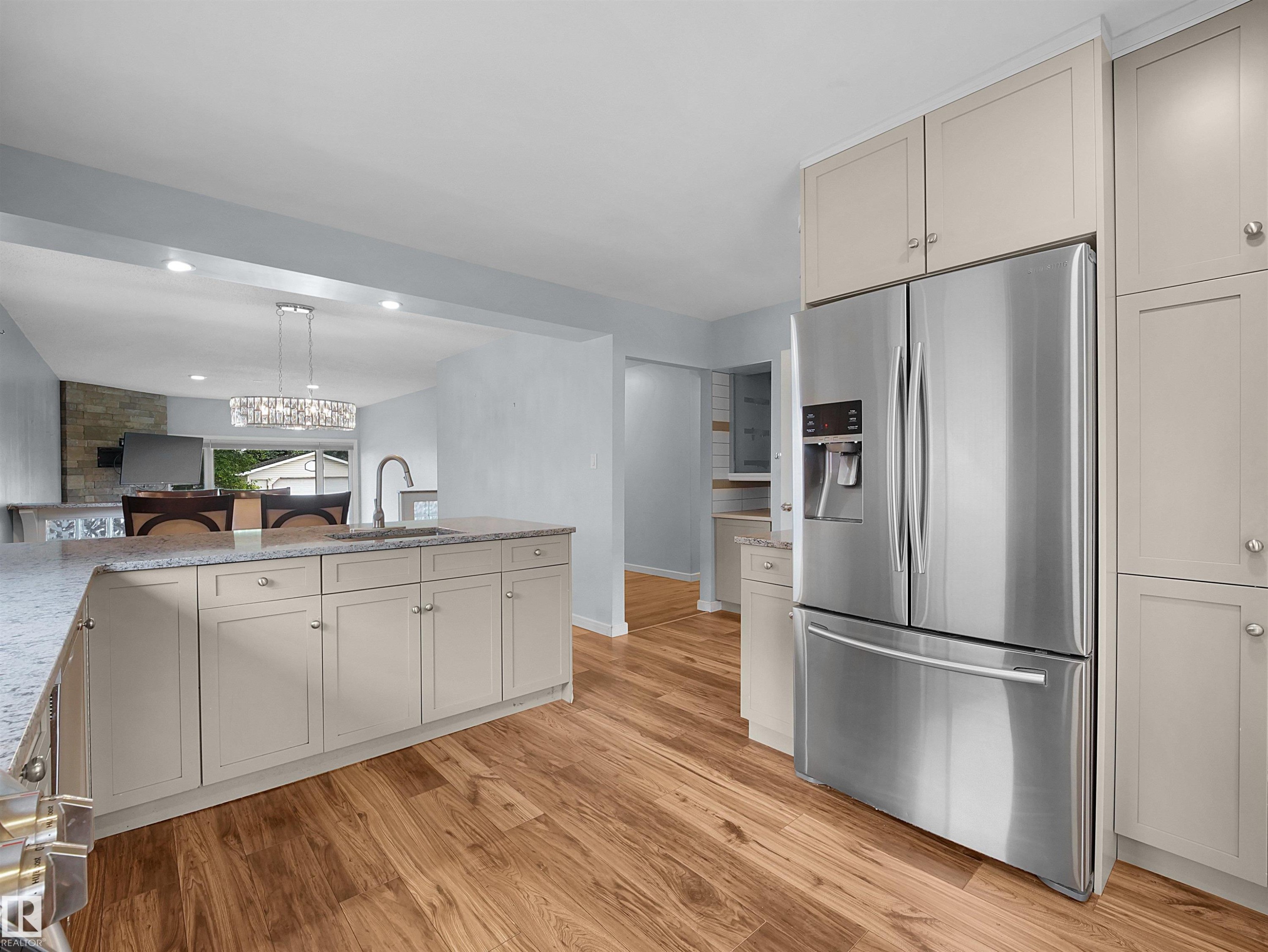 Modern kitchen featuring wood-finish flooring, light-toned cabinetry, stainless steel French door refrigerator, and a kitchen island with a basin sink and gooseneck faucet - 7435 32 Avenue Nw, Edmonton, AB
