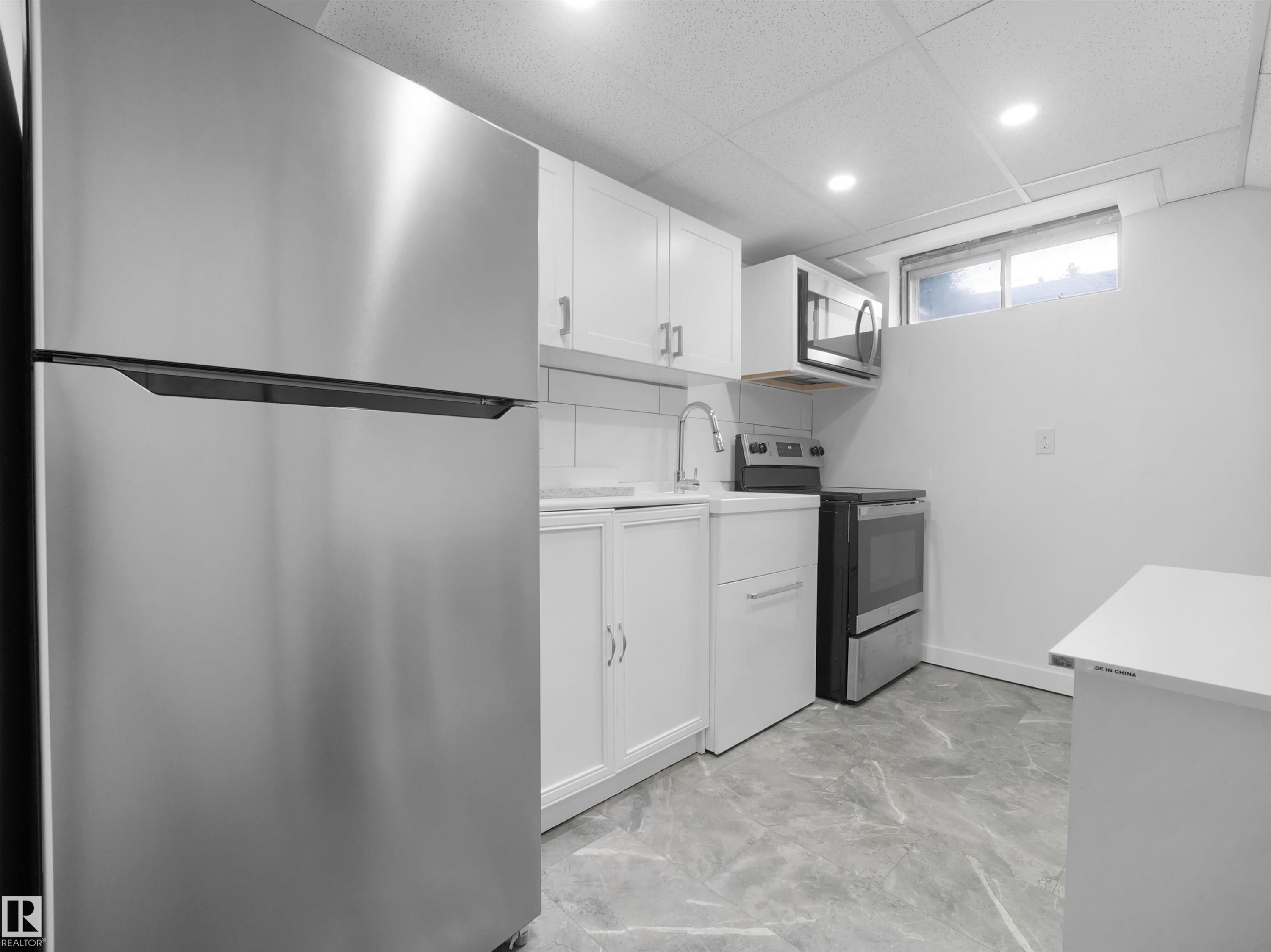 Kitchen with stainless steel appliances, white cabinetry, a built-in microwave, a stainless steel sink, and gray marble-look flooring - 7435 32 Avenue Nw, Edmonton, AB