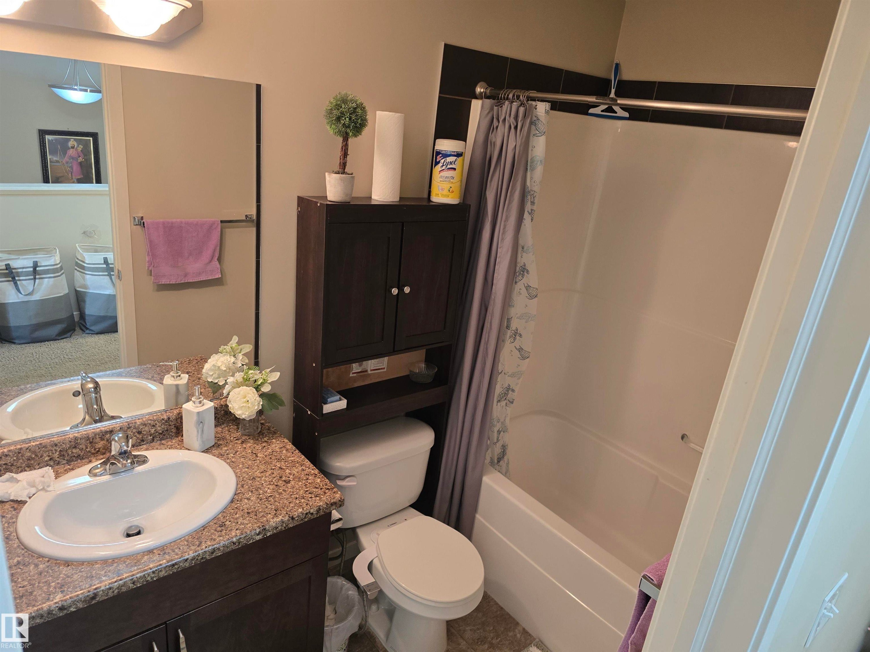 Vanity with an integrated sink and speckled countertop, dark wood-finish cabinetry, a full-width mirror, and a built-in shower-over-tub combination - 1474 33B Street Nw, Edmonton, AB