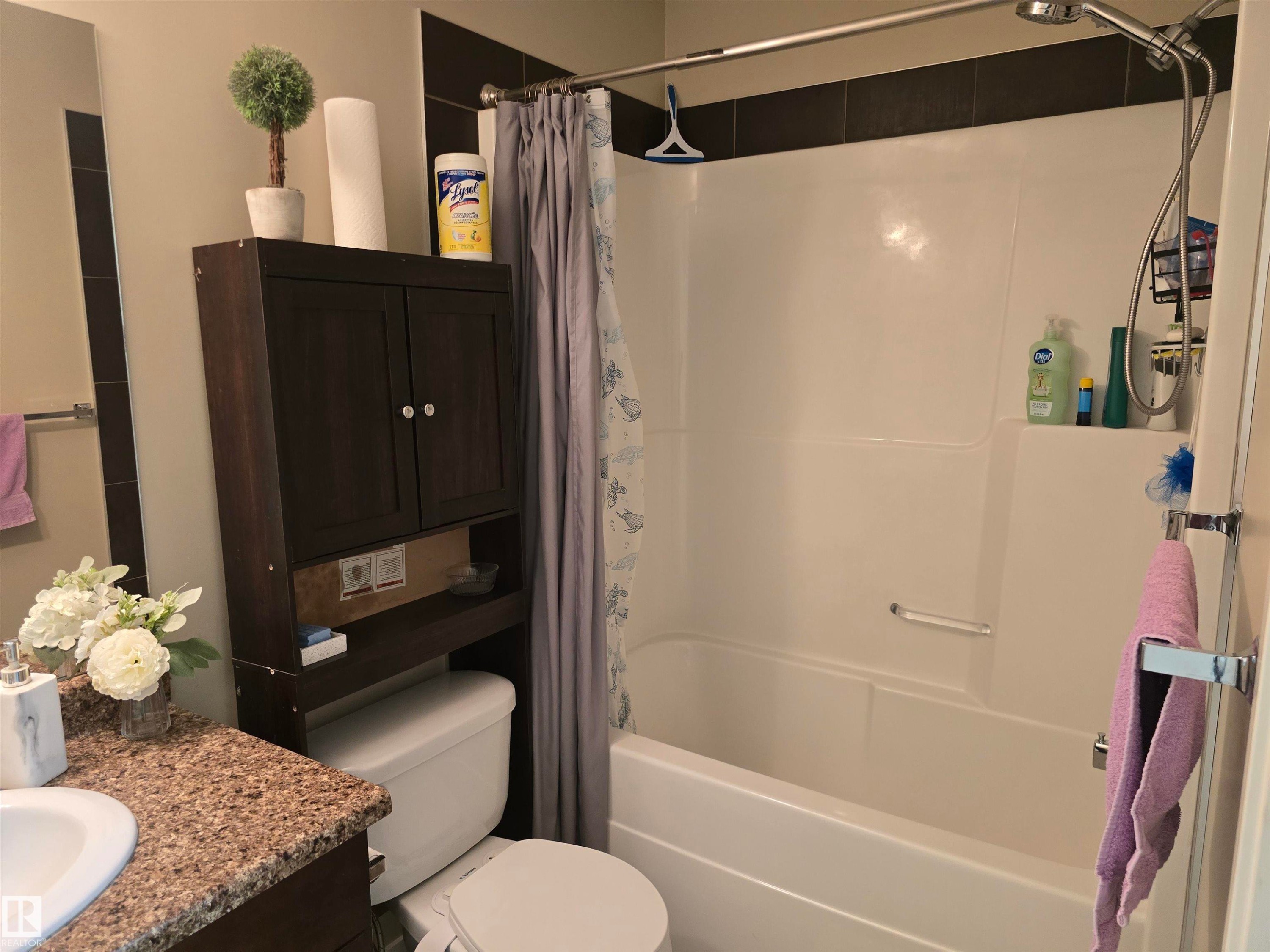 Built-in white bathtub with shower, dark wood-finish vanity with an undermount sink, speckled countertop, and a dark wood-finish over-toilet storage cabinet - 1474 33B Street Nw, Edmonton, AB