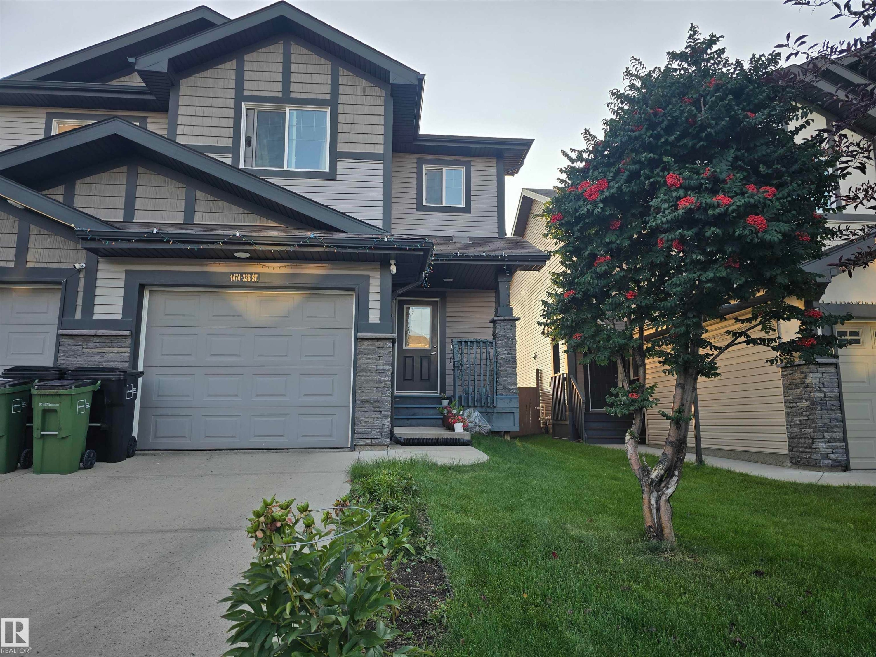 Exterior featuring a stone and siding facade, attached garage, front entryway, and a mature tree with red berries - 1474 33B Street Nw, Edmonton, AB