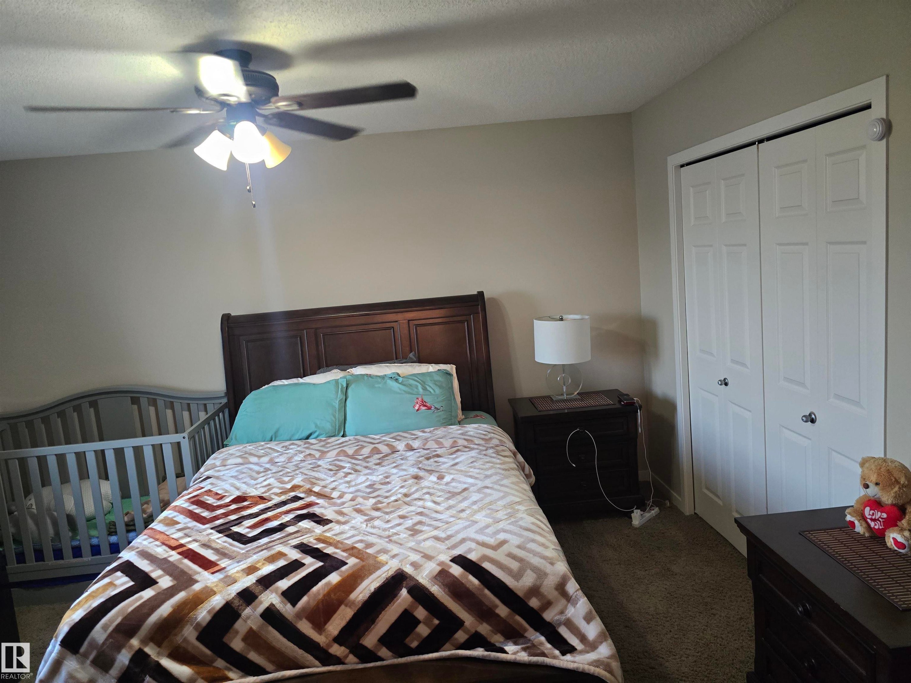 Ceiling fan with integrated lighting, wood-finish headboard, built-in closet with bi-fold doors, carpeted flooring, and neutral wall tones - 1474 33B Street Nw, Edmonton, AB