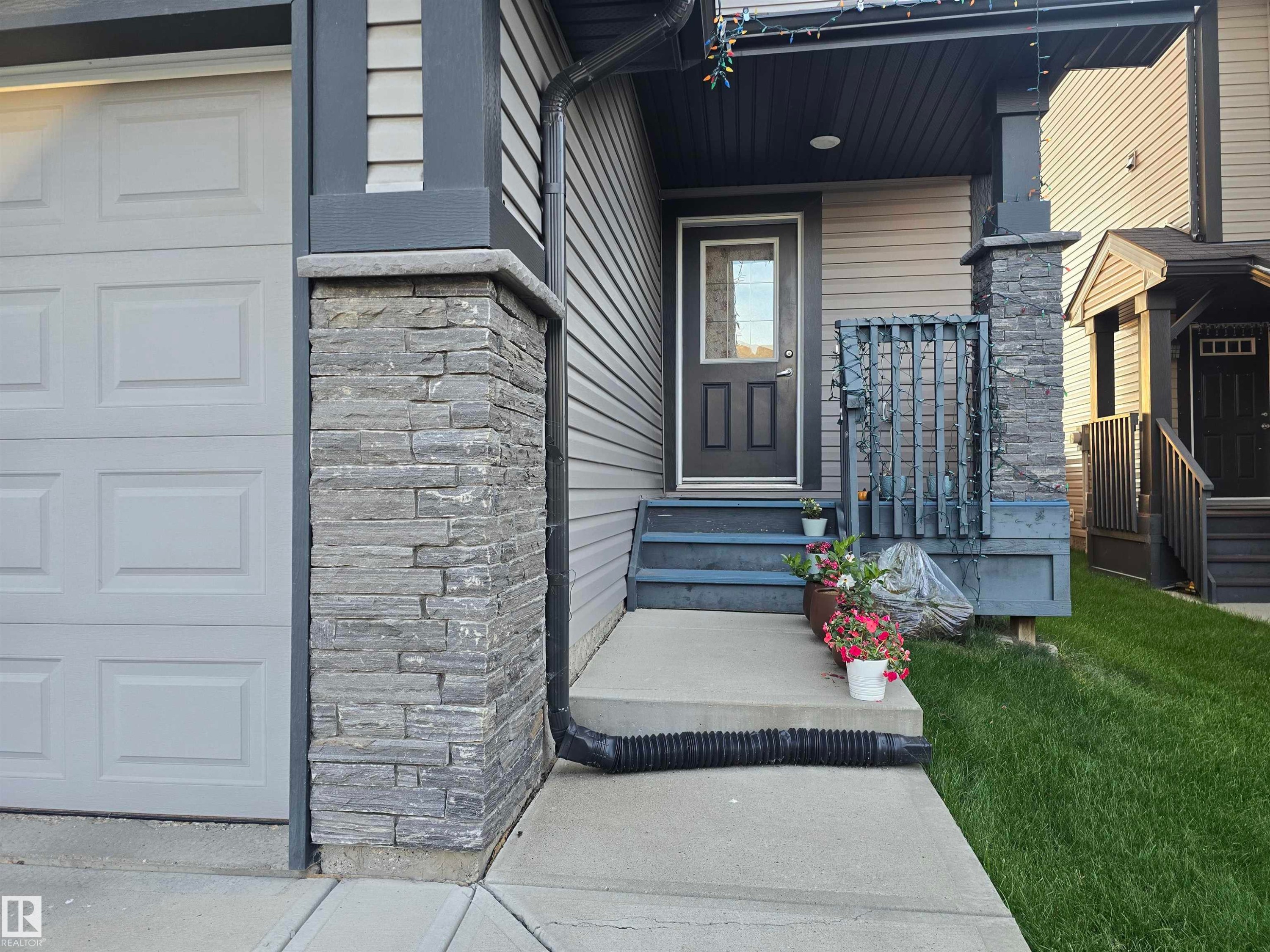 Exterior featuring horizontal siding, a paneled garage door, stacked stone accents, and a covered porch with dark wood-finish railing - 1474 33B Street Nw, Edmonton, AB