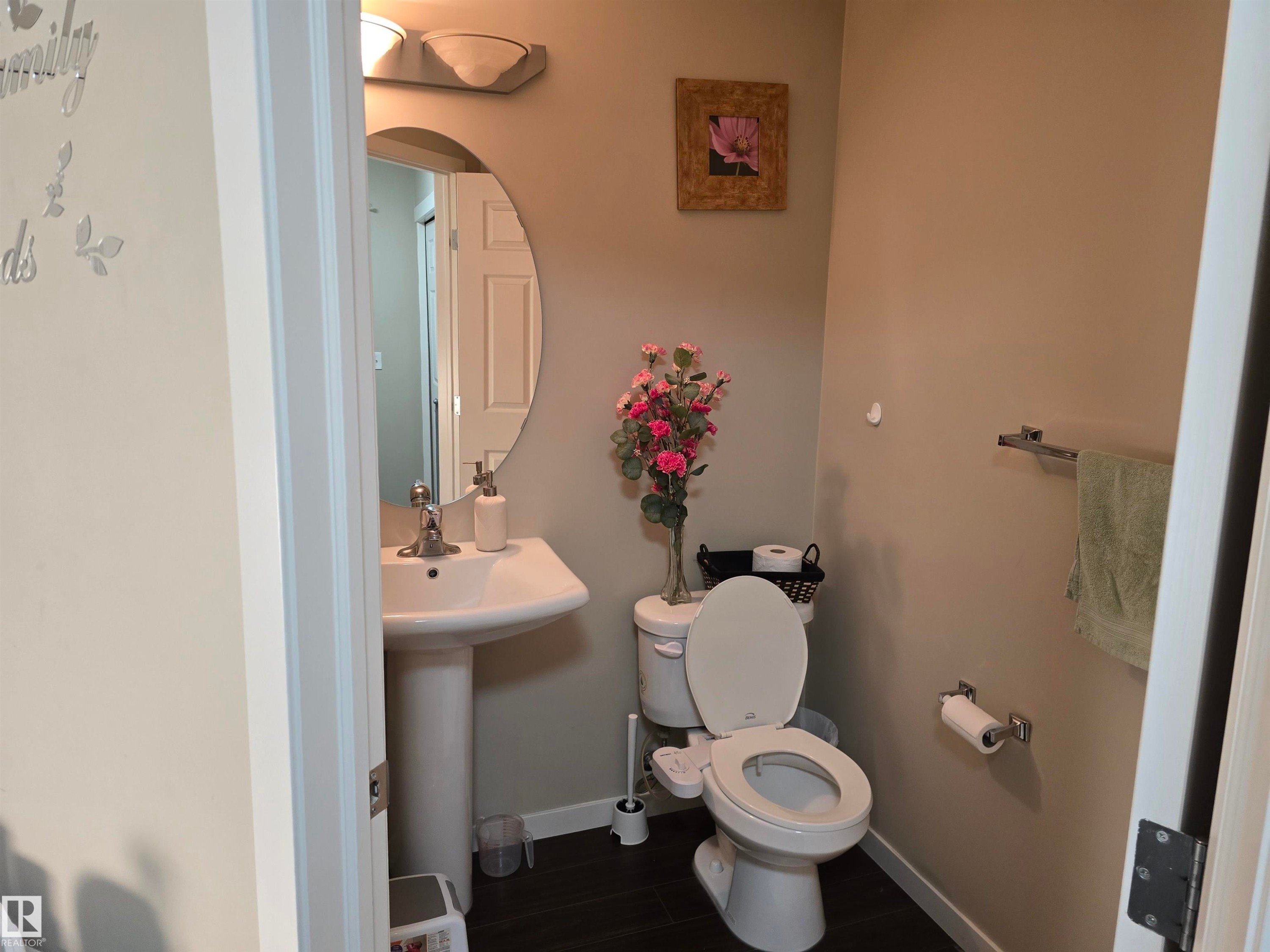 Pedestal sink with chrome-finish faucet, elongated toilet, oval mirror, and wall-mounted light fixture - 1474 33B Street Nw, Edmonton, AB
