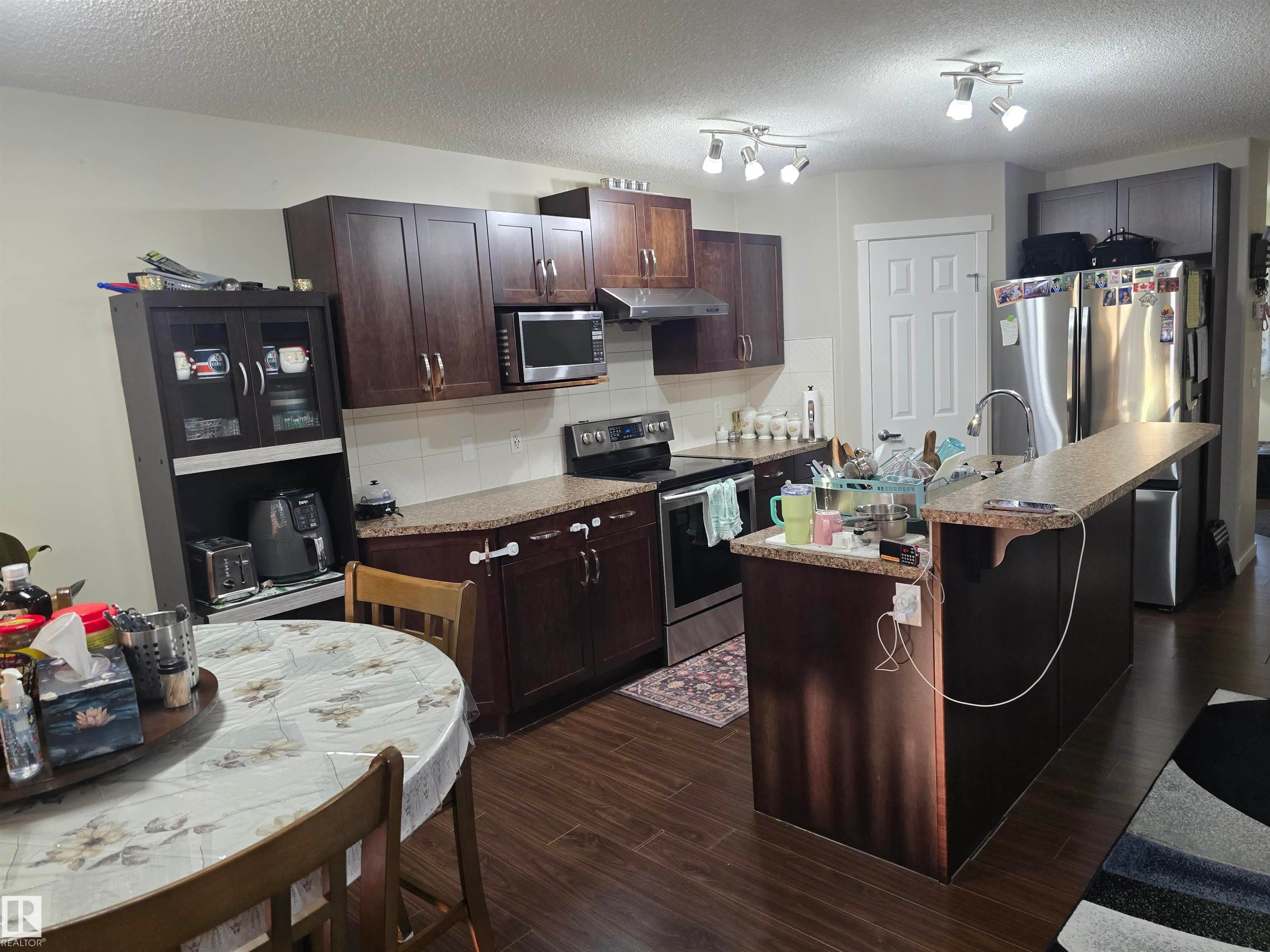 Kitchen featuring dark wood-finish cabinetry, stainless steel appliances, speckled countertops, a built-in kitchen island, and wood-finish flooring - 1474 33B Street Nw, Edmonton, AB