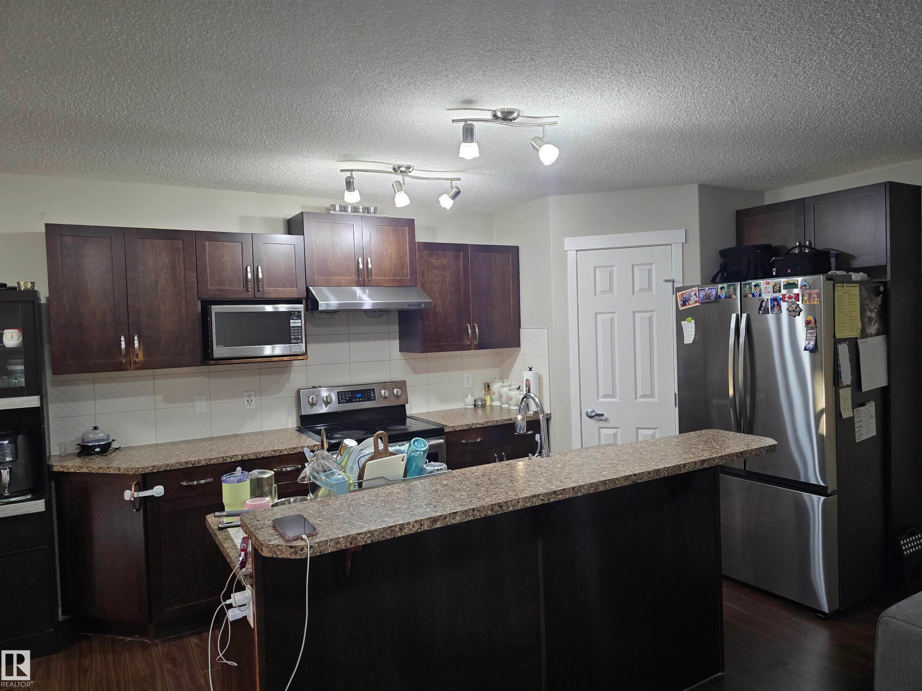 Kitchen featuring dark wood-finish cabinetry, granite-style countertops, and stainless steel appliances - 1474 33B Street Nw, Edmonton, AB