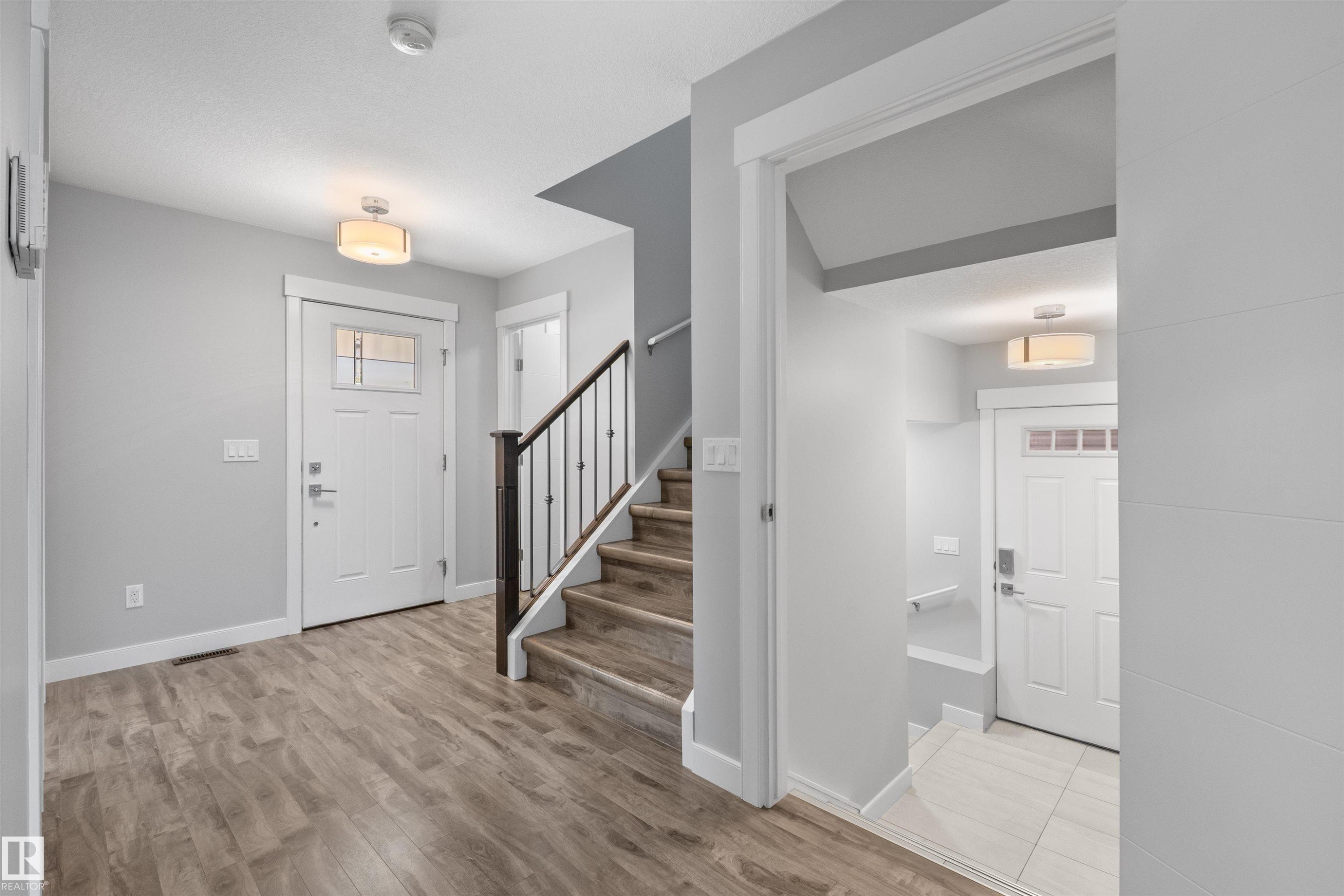 Wood-finish flooring, staircase with dark wood-finish handrail and black spindles, white interior doors, and flush mount lighting - 2585 Pegasus Boulevard Nw, Edmonton, AB