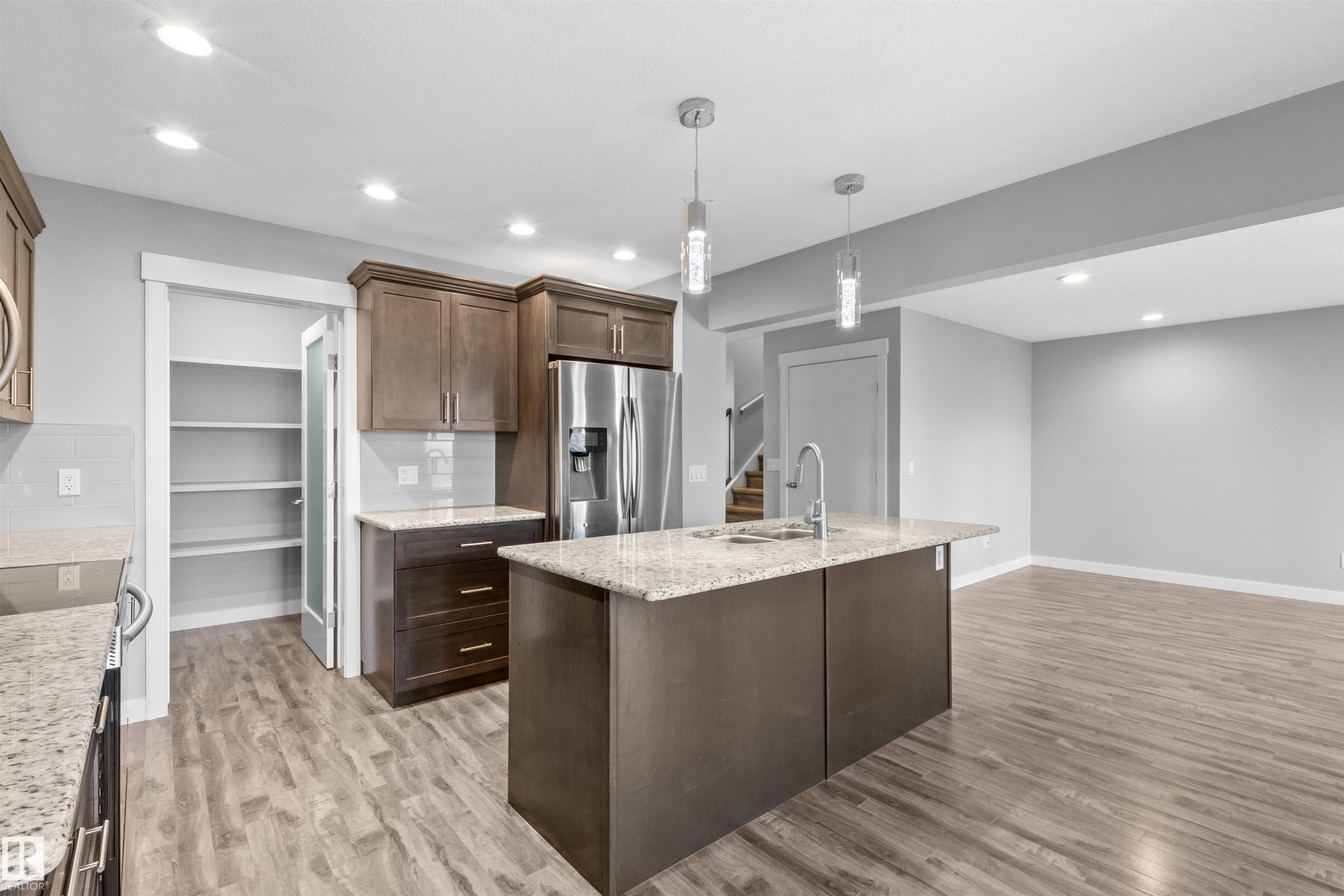 Kitchen featuring wood-finish flooring, recessed lighting, and a center island with pendant lights and a stainless steel sink - 2585 Pegasus Boulevard Nw, Edmonton, AB