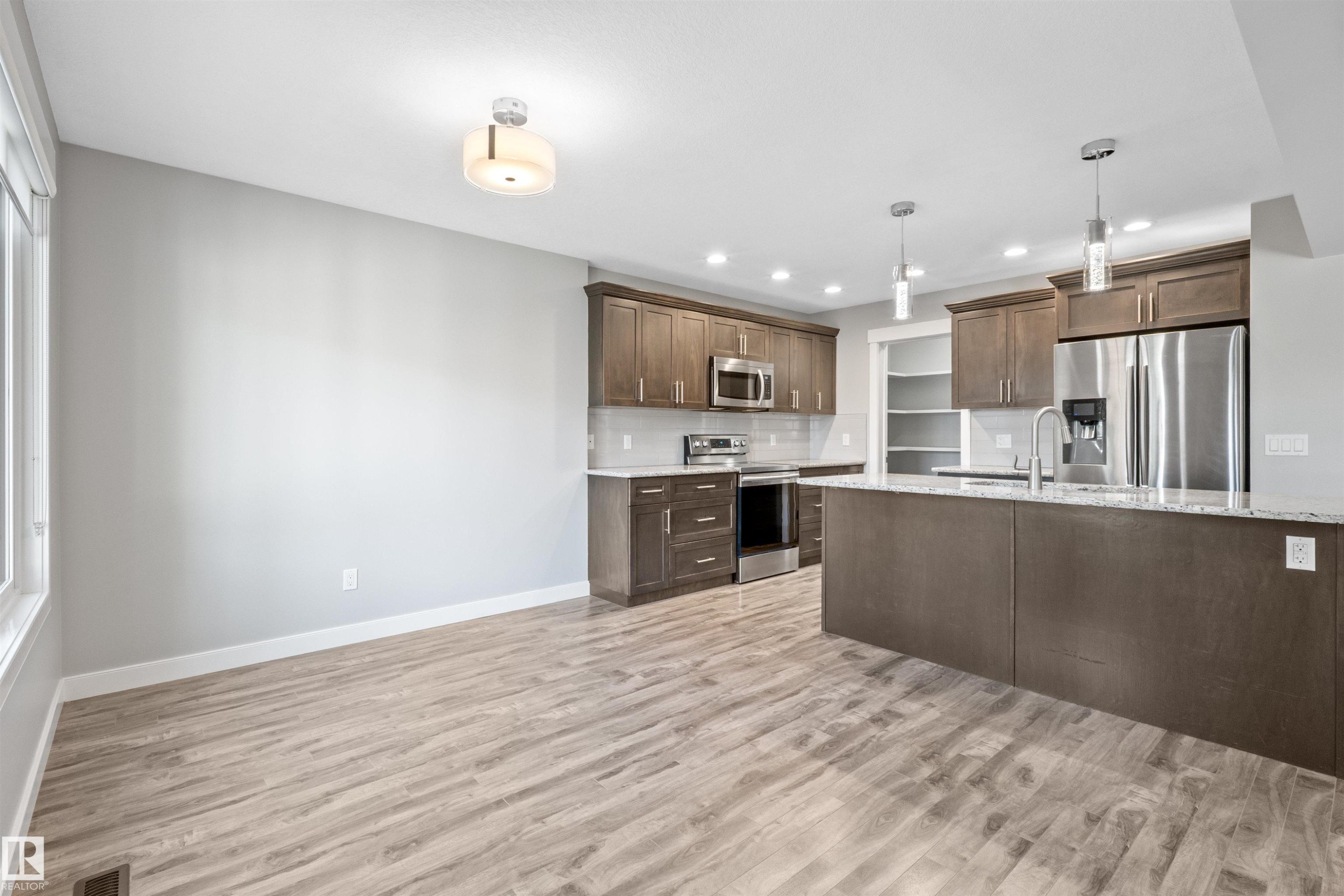Contemporary kitchen featuring stainless steel appliances, a large island with sink, pendant lighting, recessed lighting, and wood-finish flooring - 2585 Pegasus Boulevard Nw, Edmonton, AB