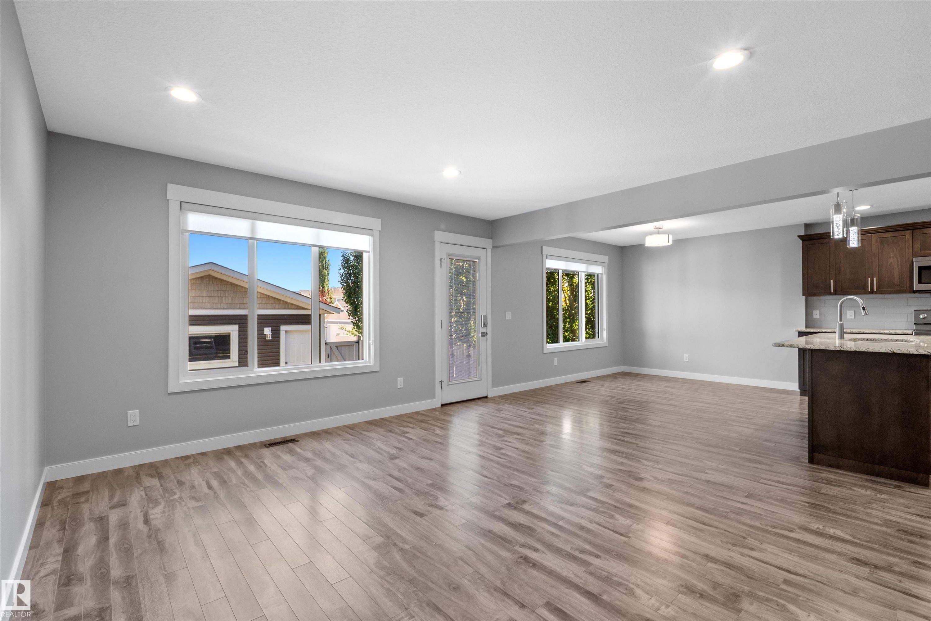 Open-concept living space with wood-finish flooring, recessed lighting, and large windows - 2585 Pegasus Boulevard Nw, Edmonton, AB