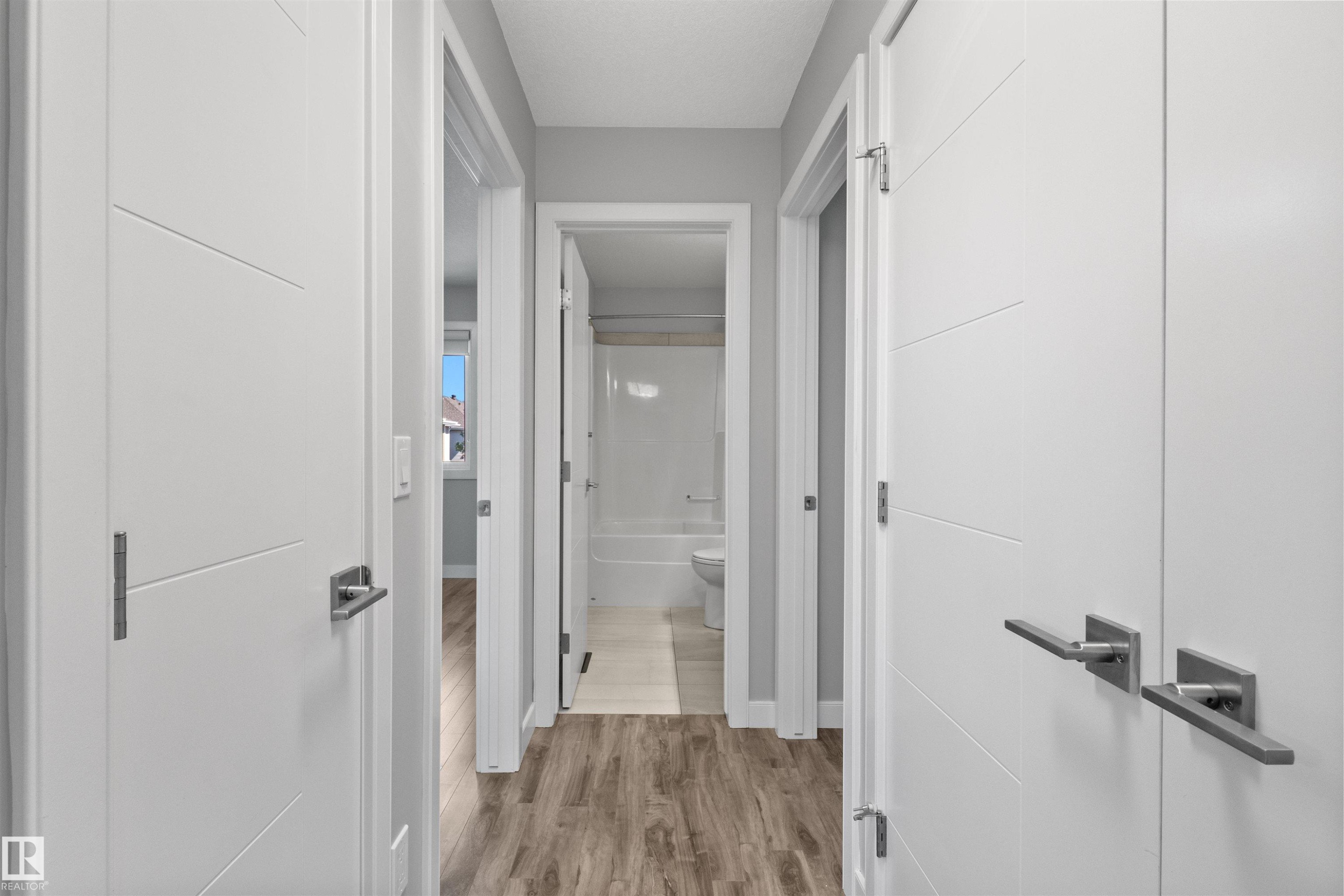 Hallway featuring wood-finish flooring and modern white doors with horizontal paneling and brushed nickel hardware - 2585 Pegasus Boulevard Nw, Edmonton, AB