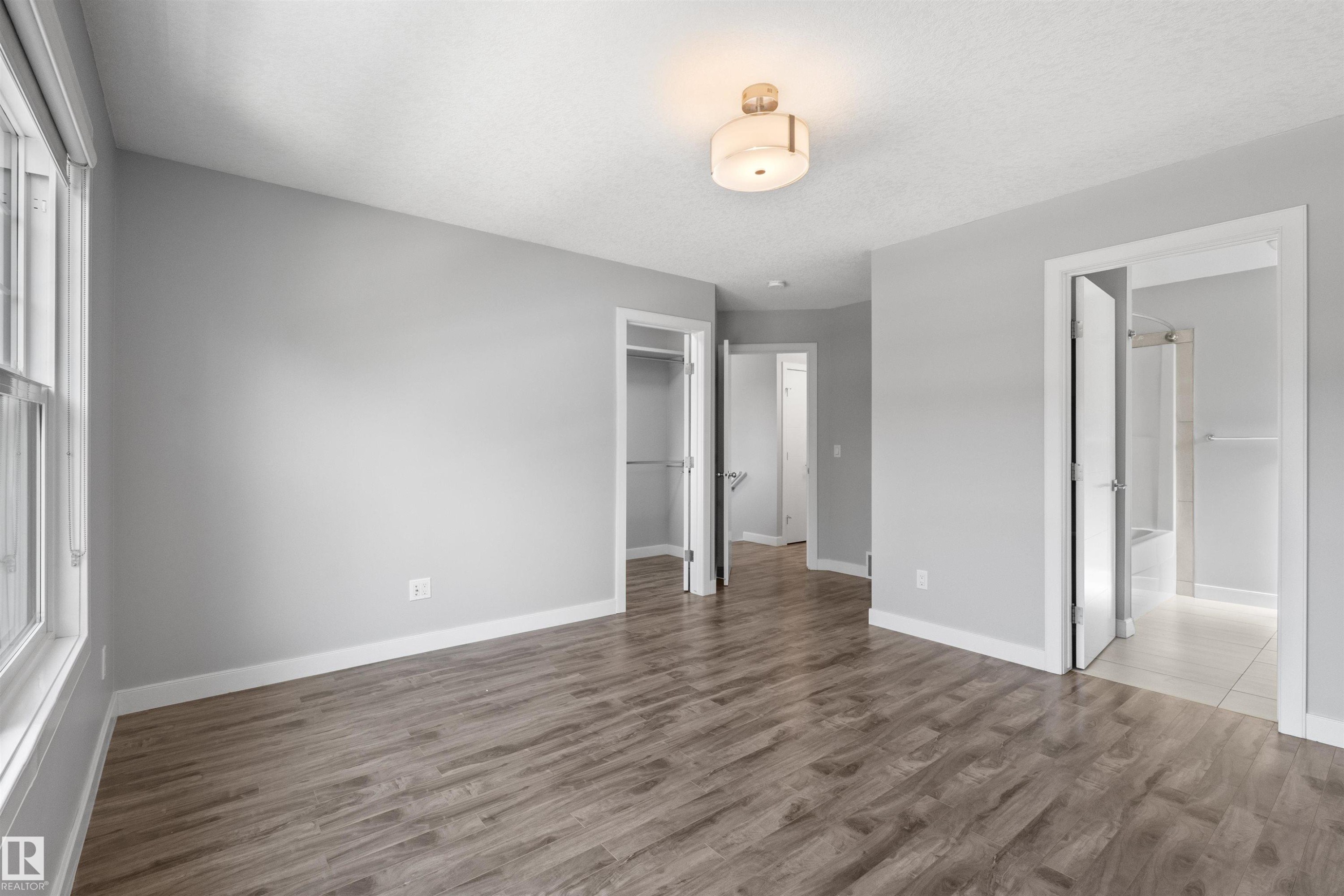Wood-finish flooring, light gray wall color, white trim throughout, flush mount ceiling fixture, and a window with white casing - 2585 Pegasus Boulevard Nw, Edmonton, AB