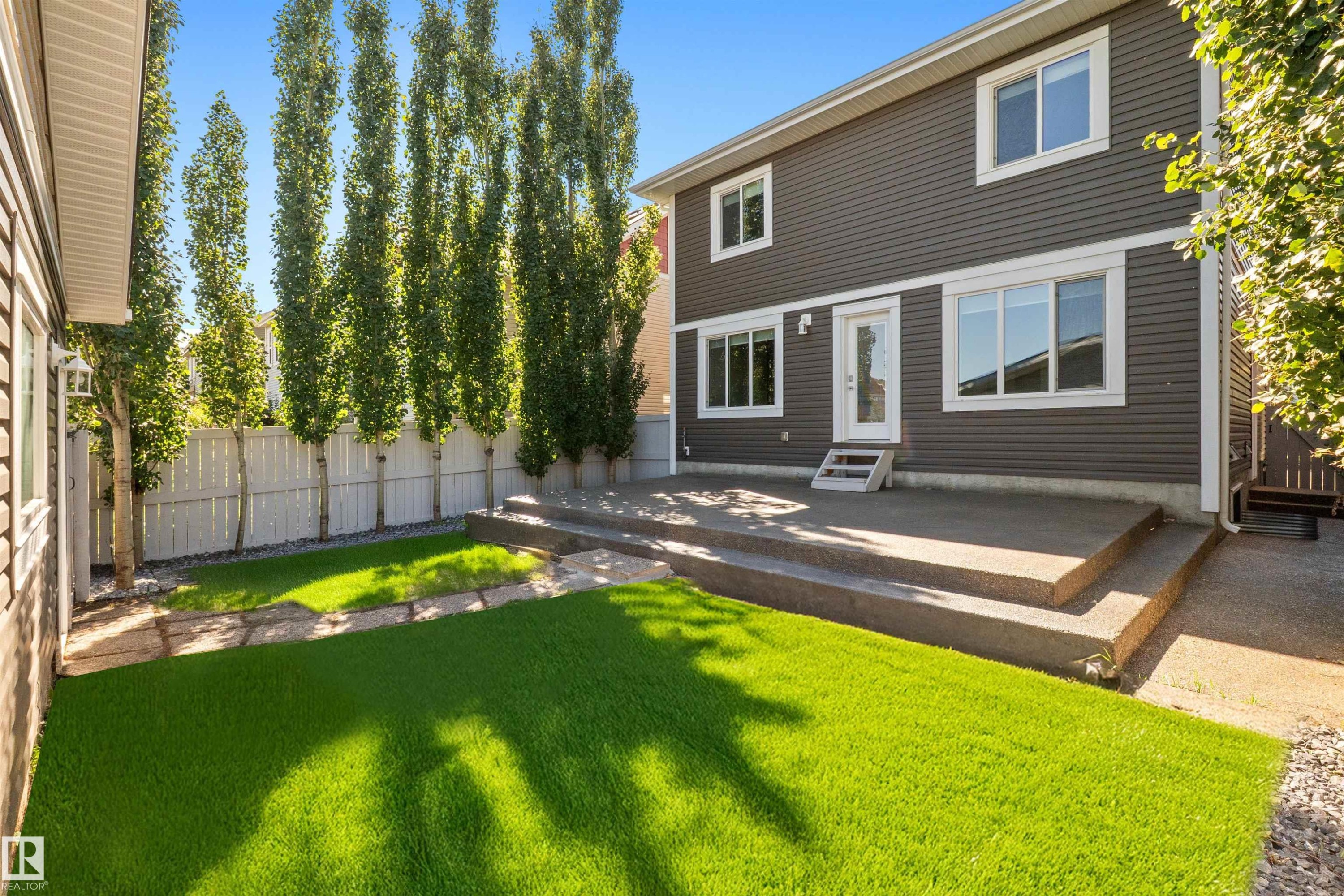 Expansive backyard featuring artificial turf, a multi-level concrete patio, and a white privacy fence - 2585 Pegasus Boulevard Nw, Edmonton, AB