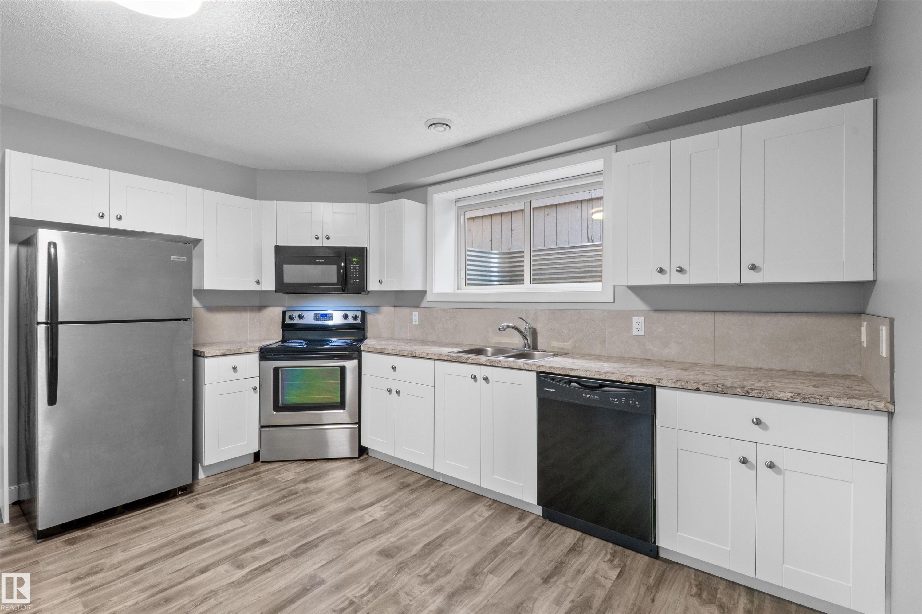 Wood-finish flooring with white shaker-style cabinetry, stainless steel refrigerator, stainless steel range, and a black dishwasher - 2585 Pegasus Boulevard Nw, Edmonton, AB