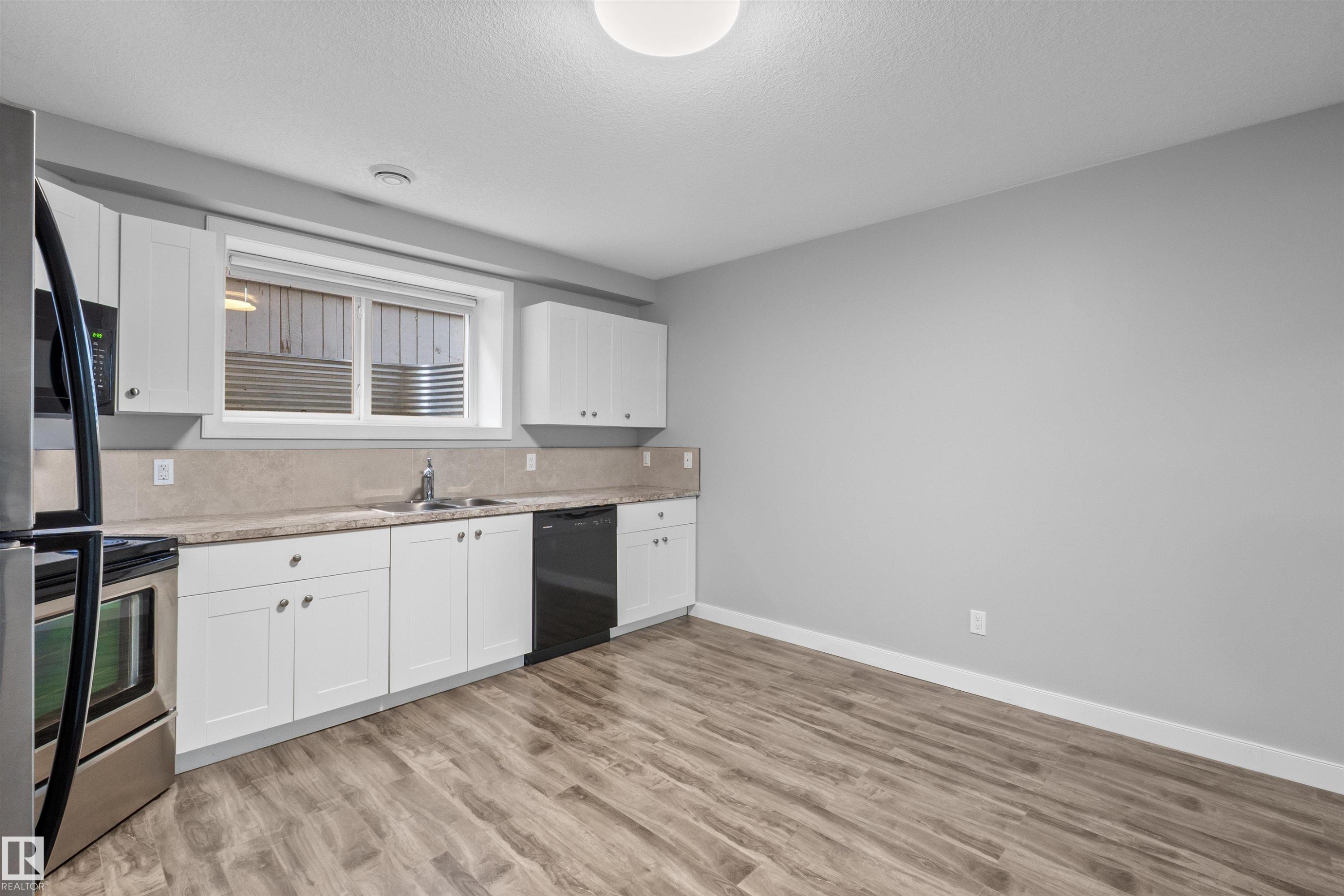 Kitchen area featuring white cabinetry, stainless steel appliances, wood-finish flooring, and a window with a stone-finish backsplash - 2585 Pegasus Boulevard Nw, Edmonton, AB