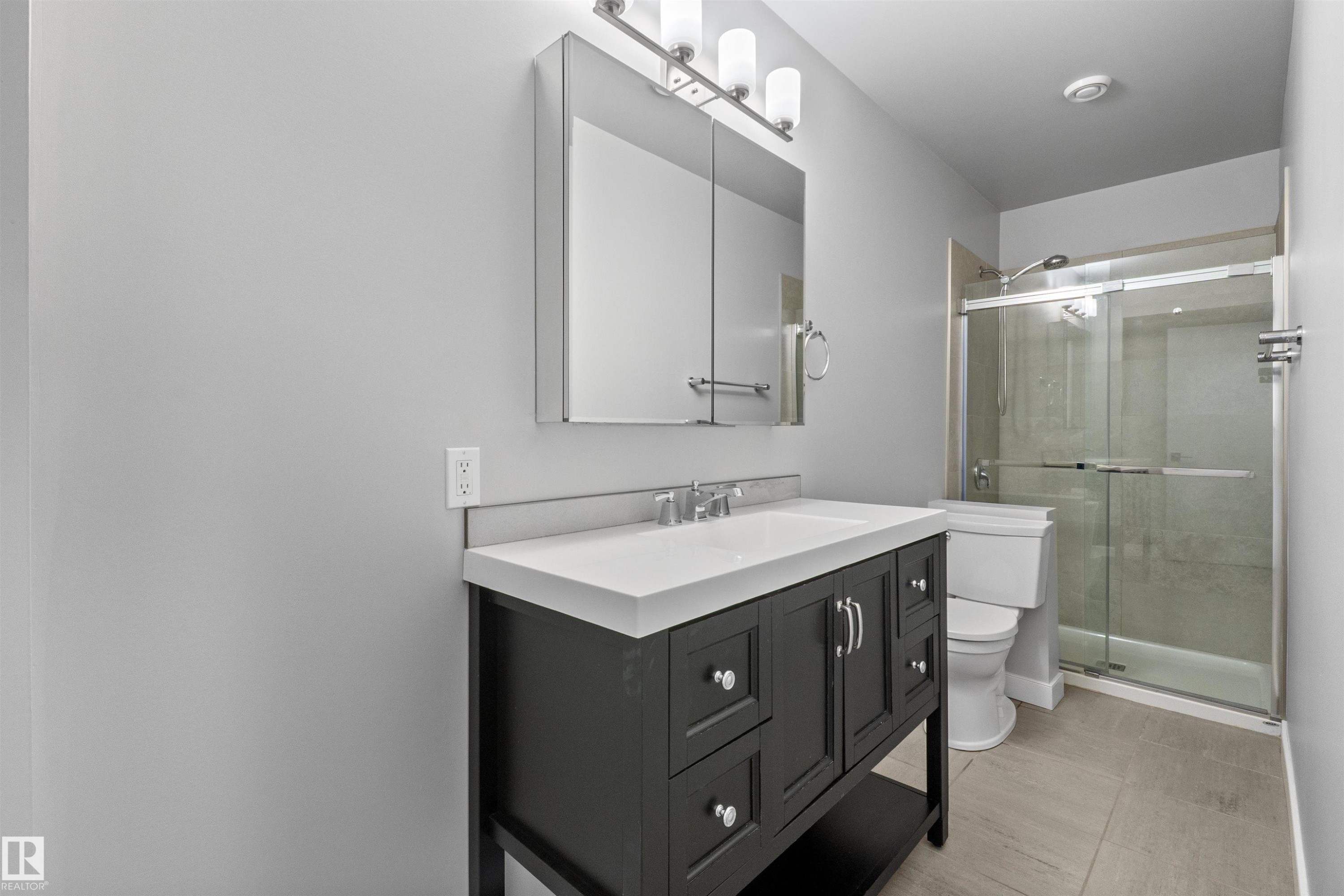 Bathroom featuring a single vanity with a dark wood-finish cabinet, white countertop, and a medicine cabinet with integrated lighting - 2585 Pegasus Boulevard Nw, Edmonton, AB