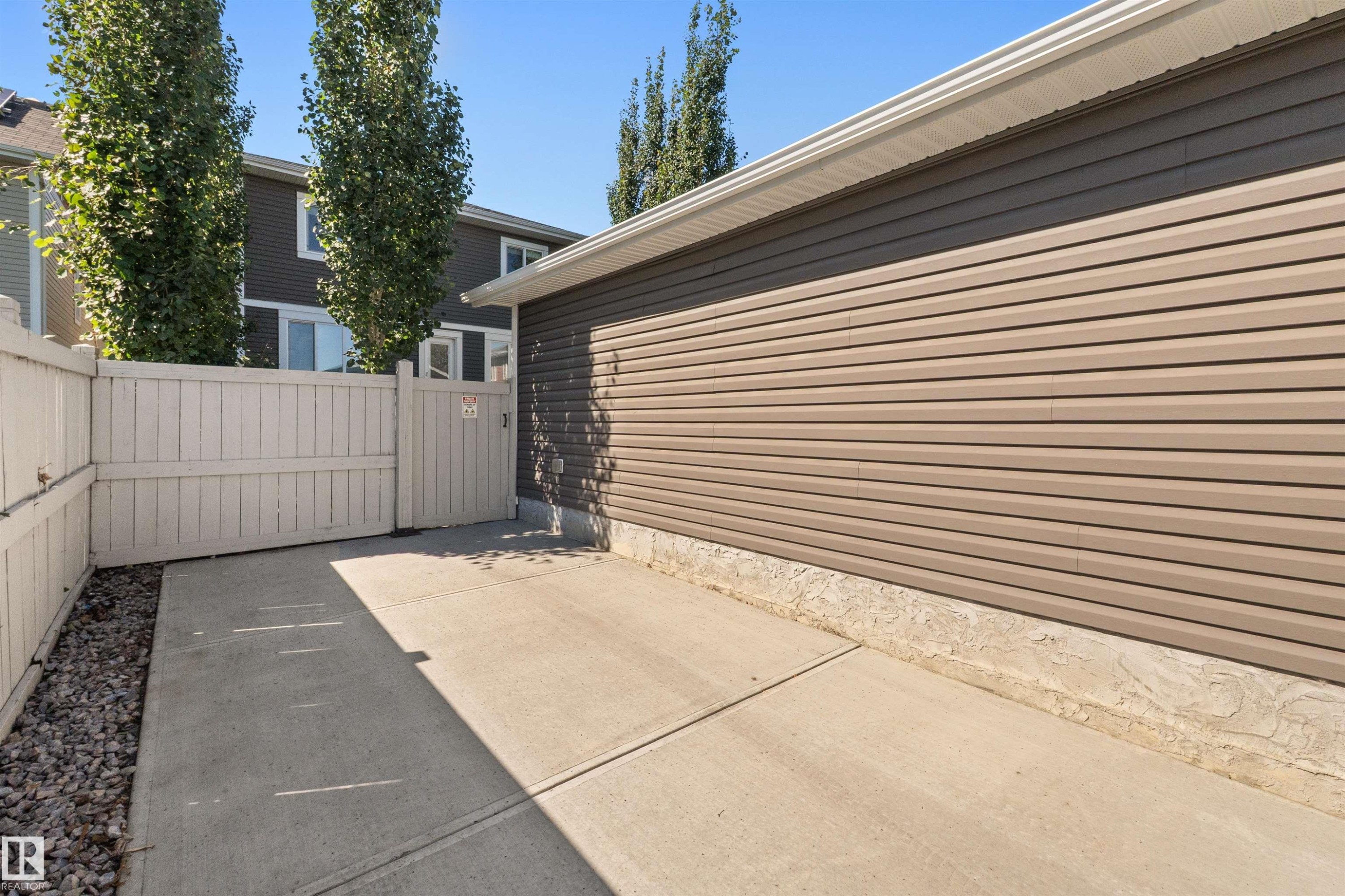 Concrete pad with gravel border, alongside a light-colored privacy fence with gate, and building with horizontal siding - 2585 Pegasus Boulevard Nw, Edmonton, AB