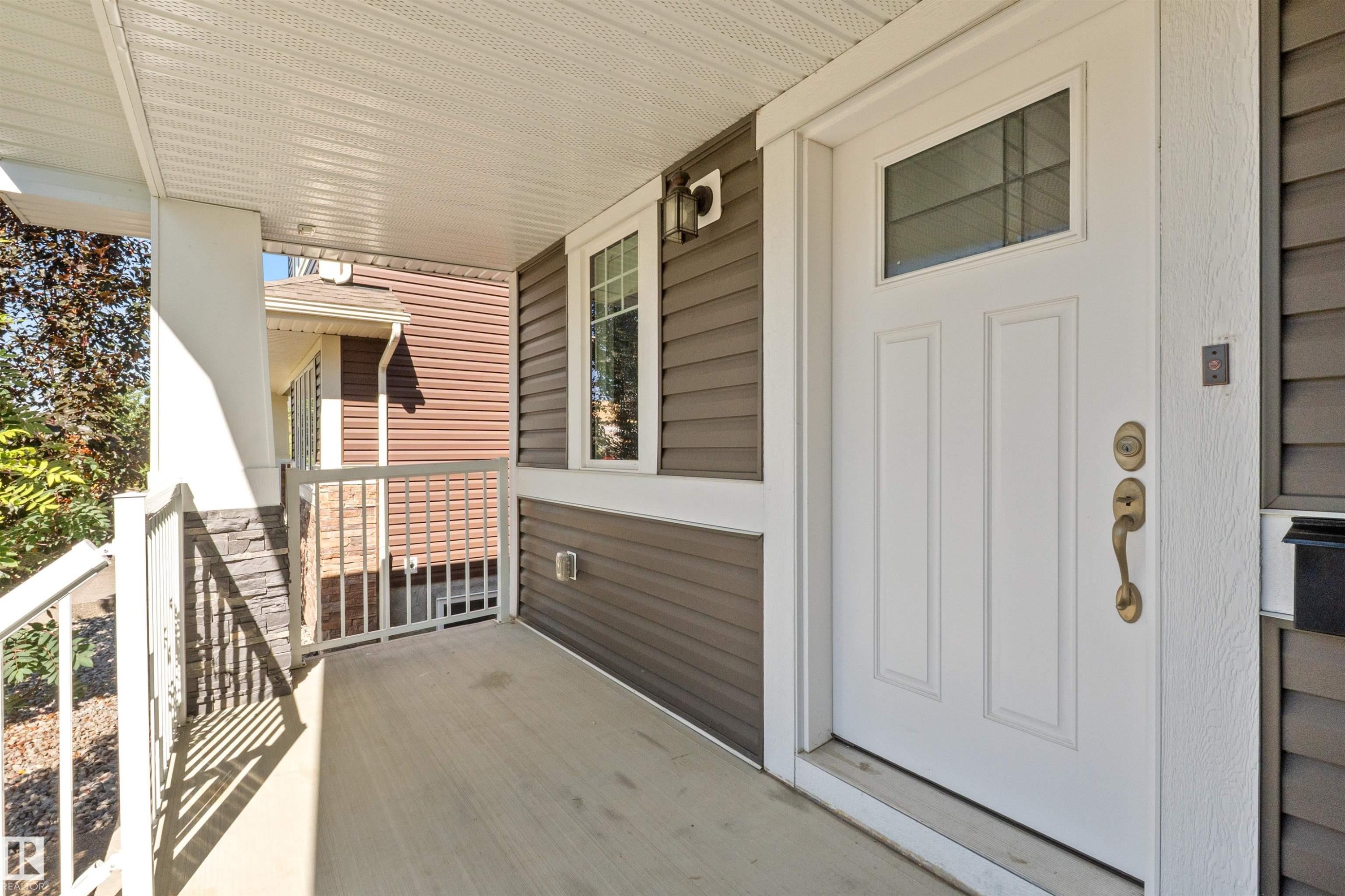 Covered porch with concrete flooring, white column, decorative stone paneling, and white railing - 2585 Pegasus Boulevard Nw, Edmonton, AB