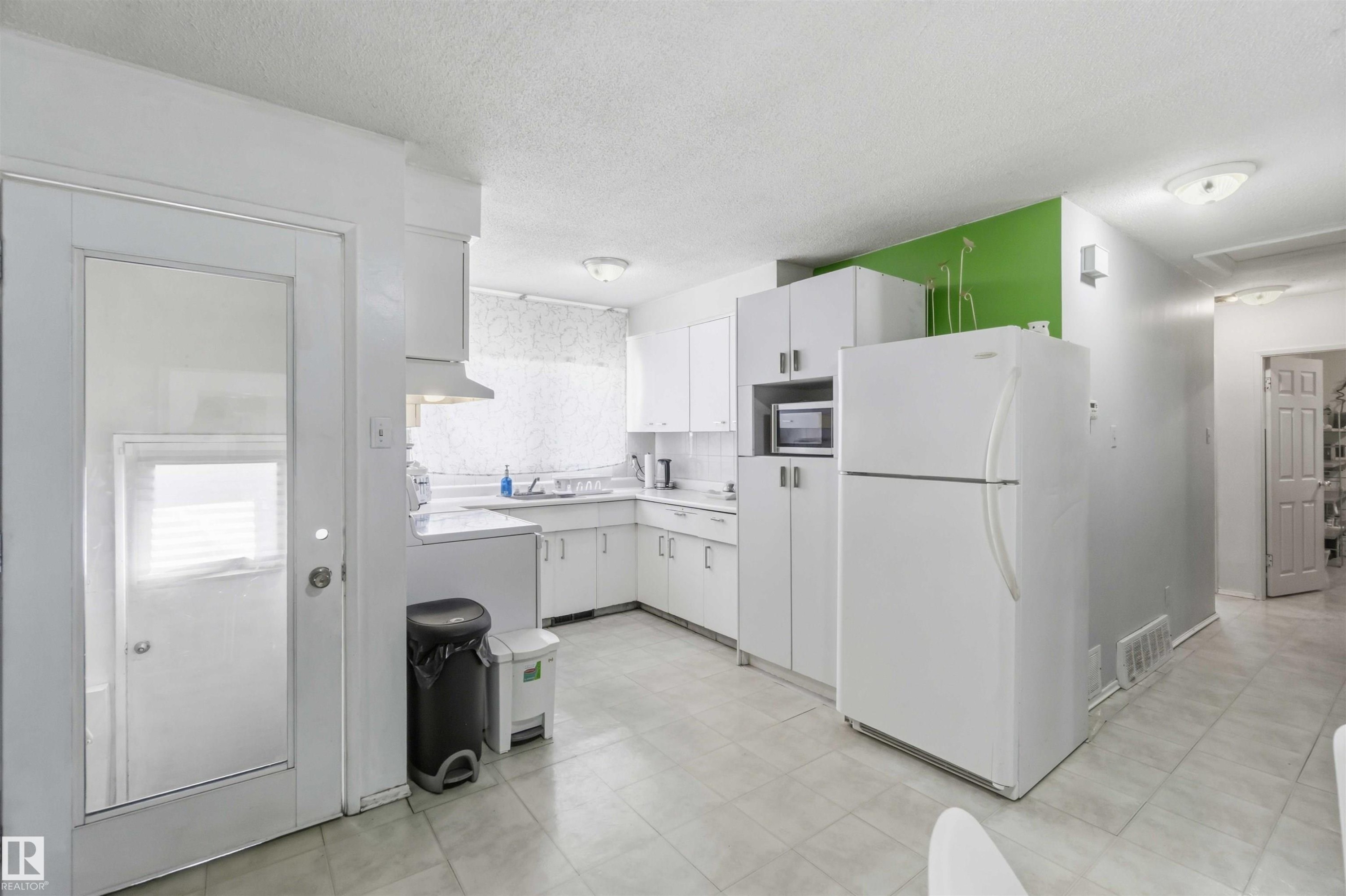 Kitchen featuring white cabinetry, white appliances, a tile floor, and a corner sink - 13408 67 Street Nw, Edmonton, AB